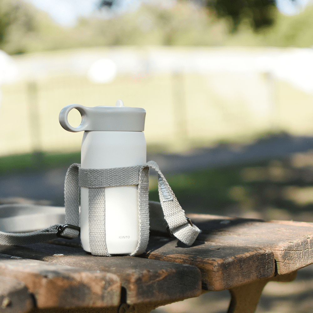 White water bottle with gray strap on a wooden picnic table outdoors.
