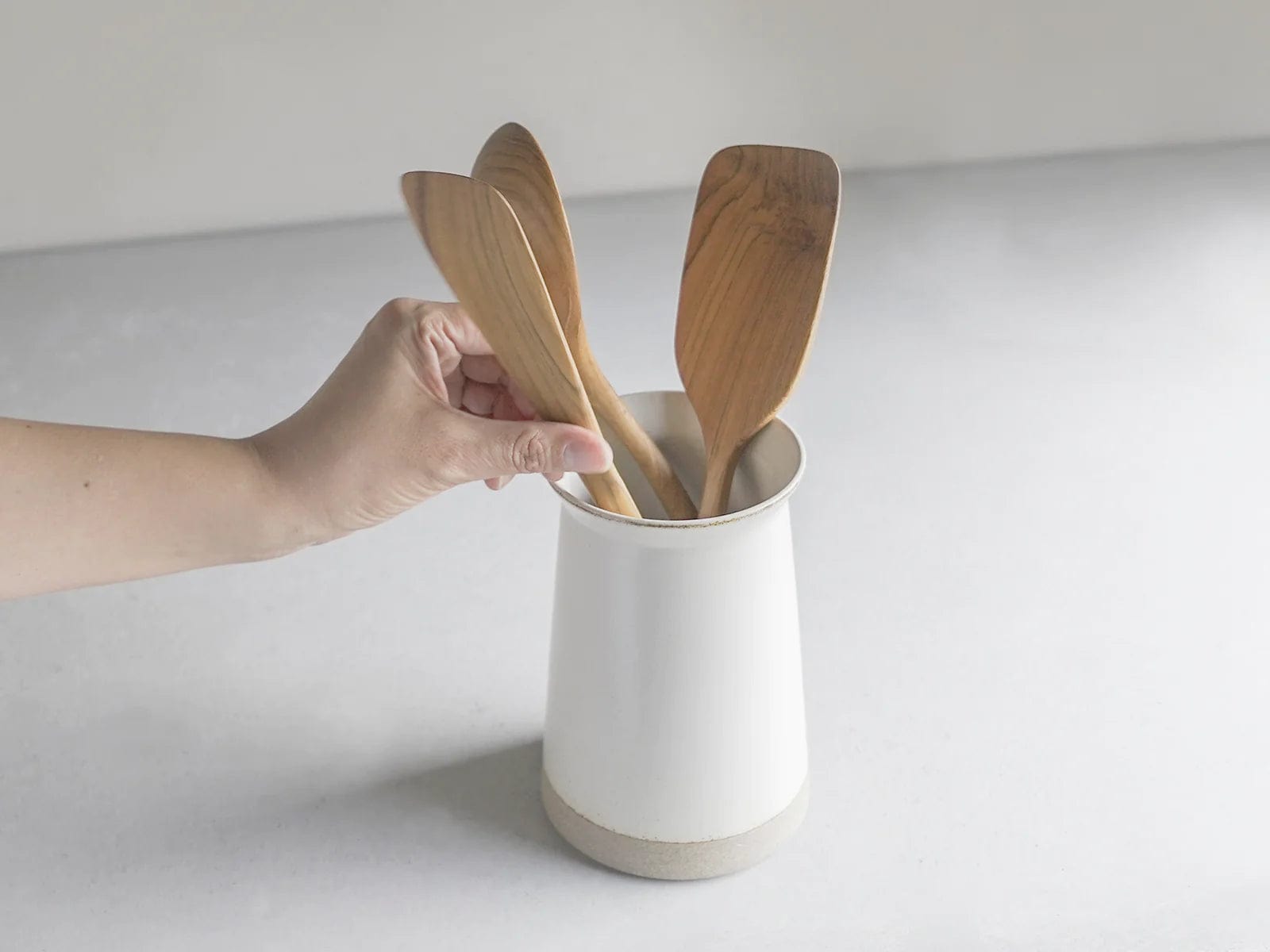 A hand placing wooden utensils into a white ceramic holder.