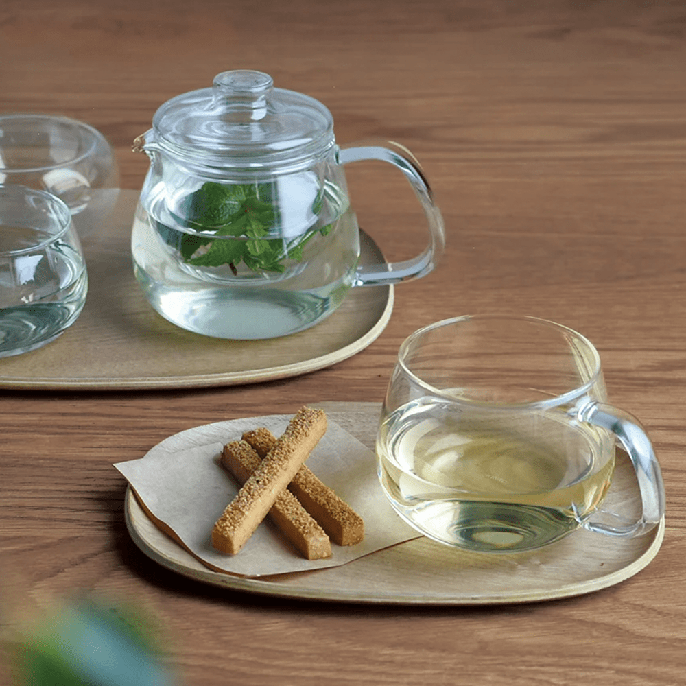Glass teapot and cup with mint tea on a wooden tray with biscotti sticks.