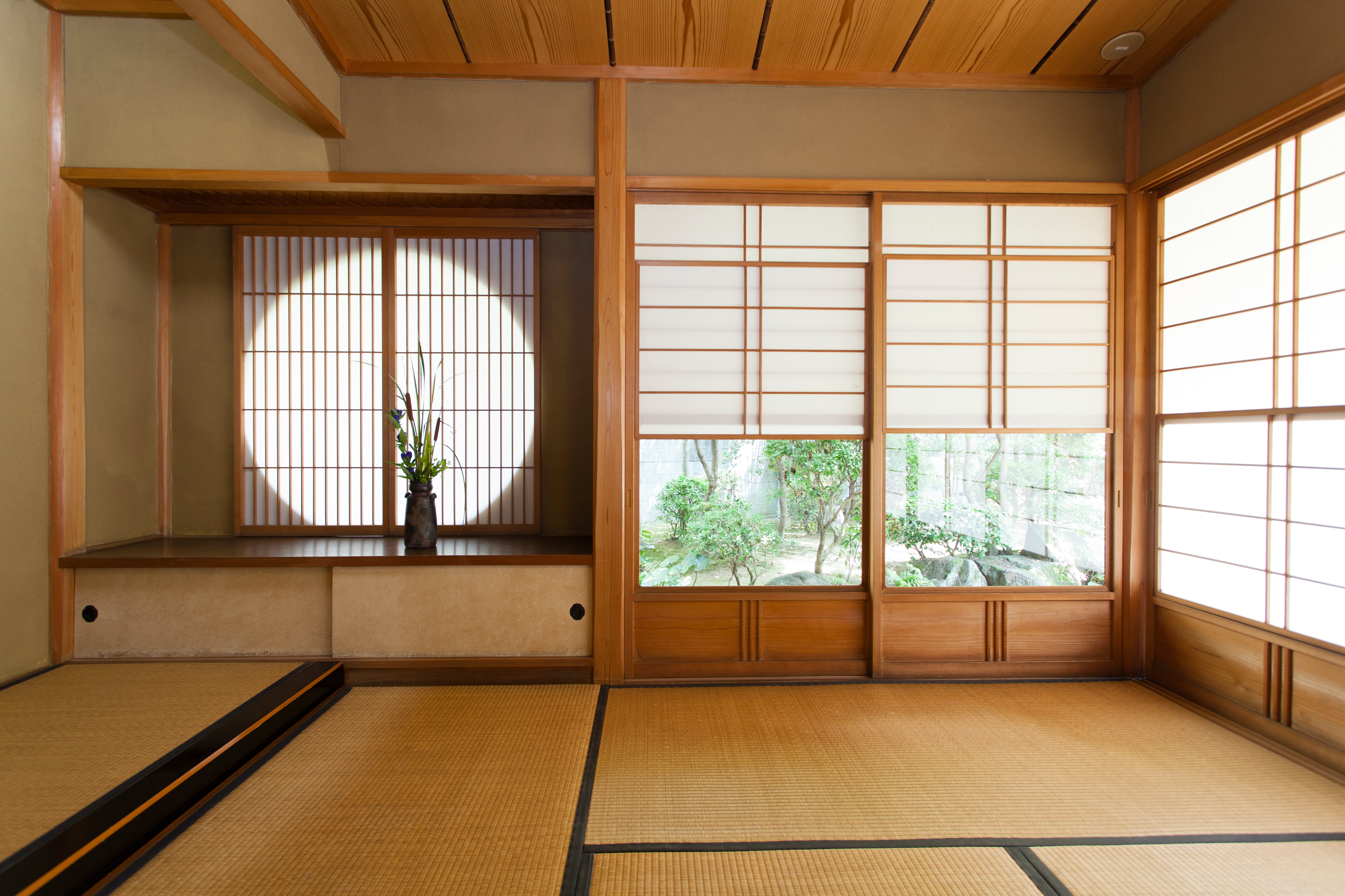 Traditional Japanese room with tatami mats, wooden ceiling, and round window with a vase of flowers.