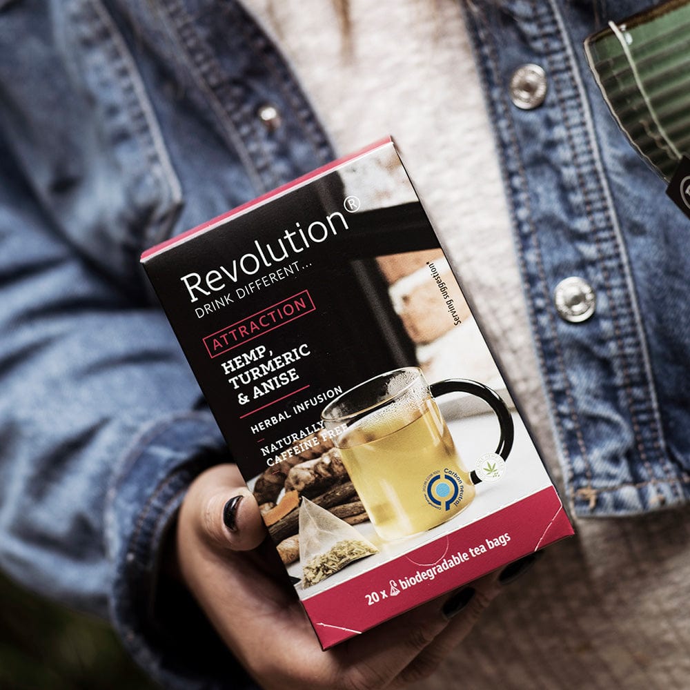 Person holding a box of Hemp, Turmeric and Anise Attraction tea against denim jacket.