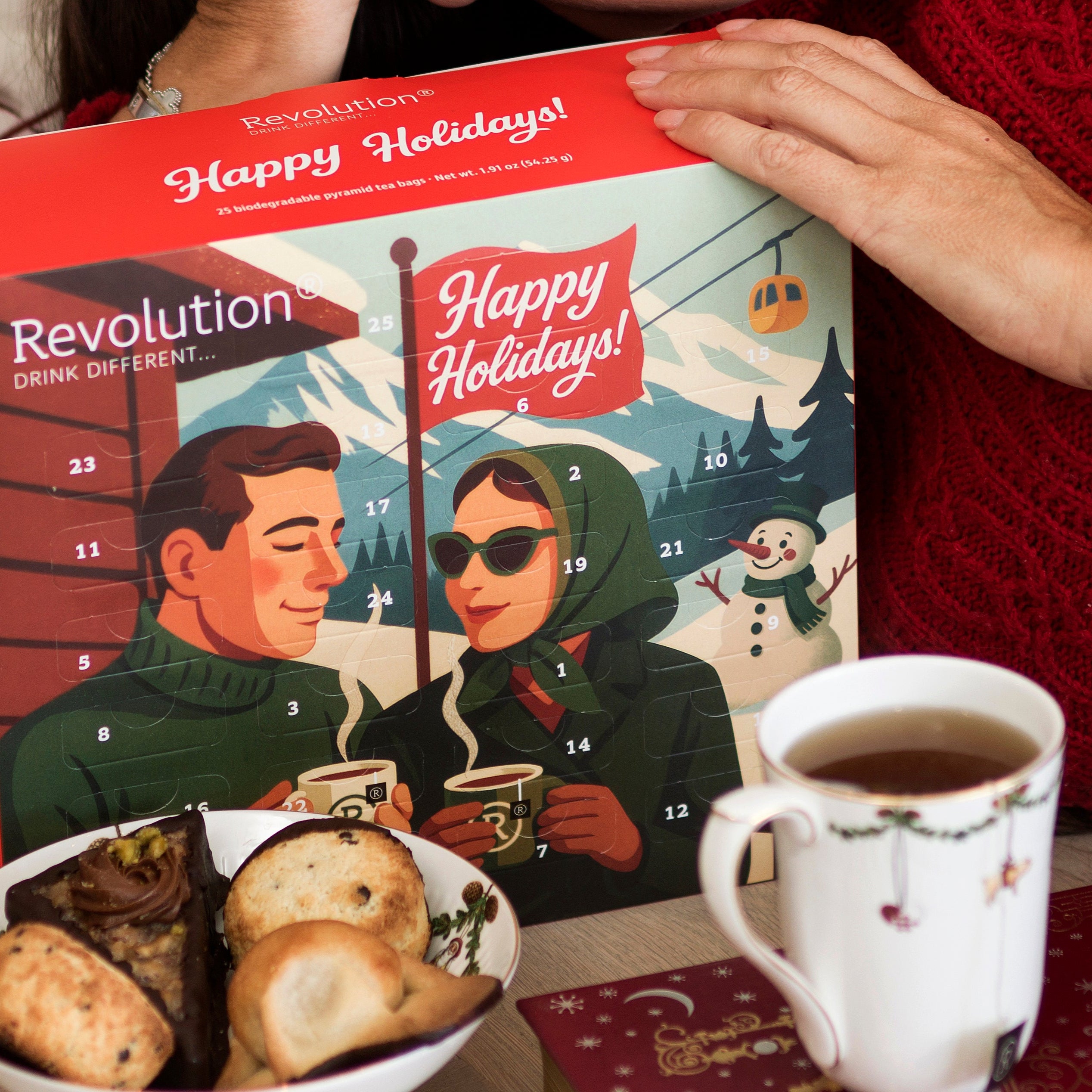 Person lifting a Happy Holidays advent calendar with illustrated couple sipping drinks.