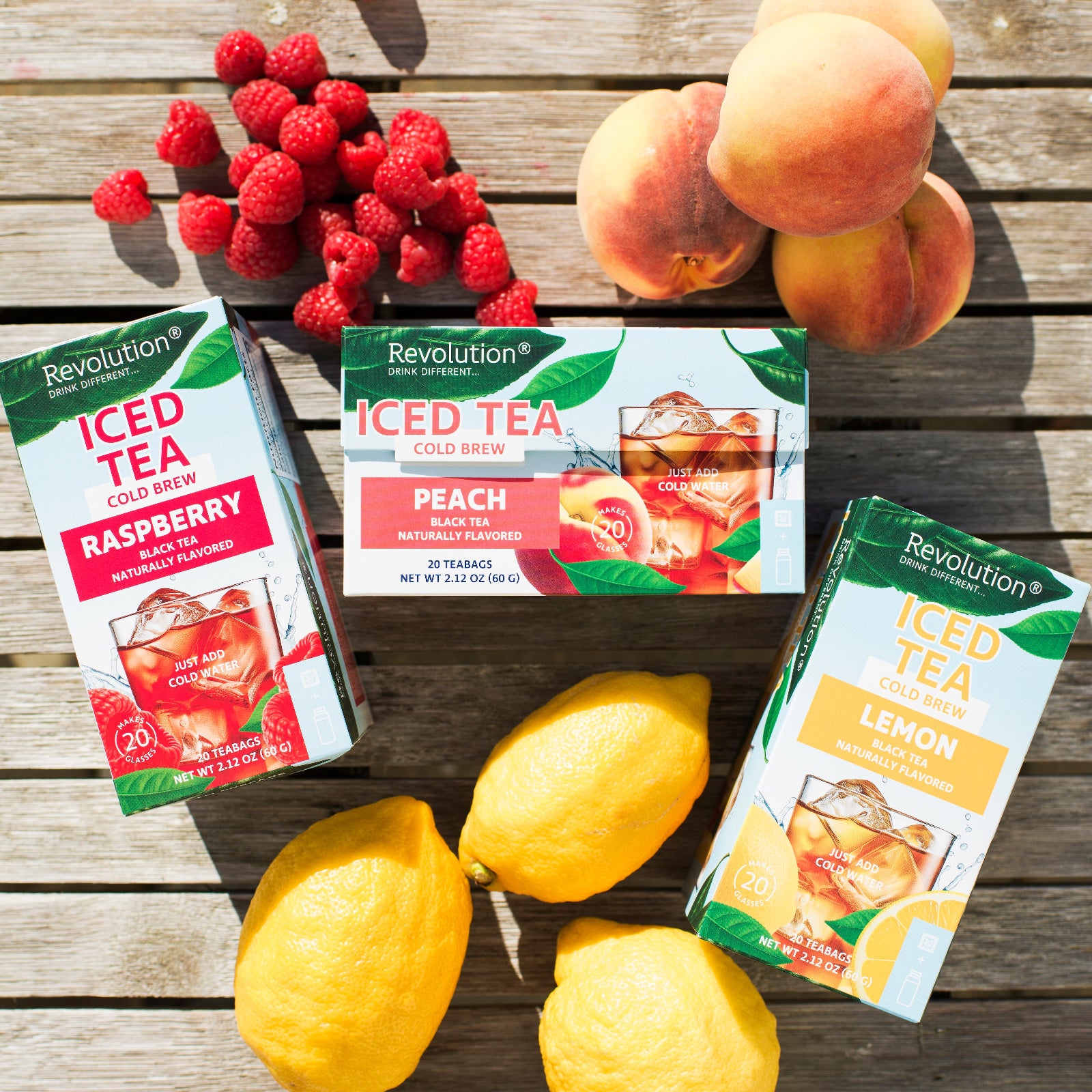 Three boxes of Revolution Iced Tea with raspberry, peach, and lemon flavors on a wooden surface with lemons and raspberries.