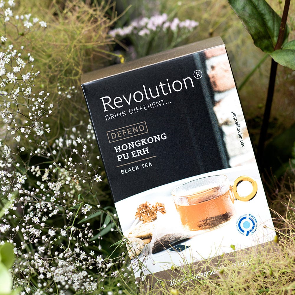 Box of Hong Kong Pu Erh black tea among green plants with small white flowers.