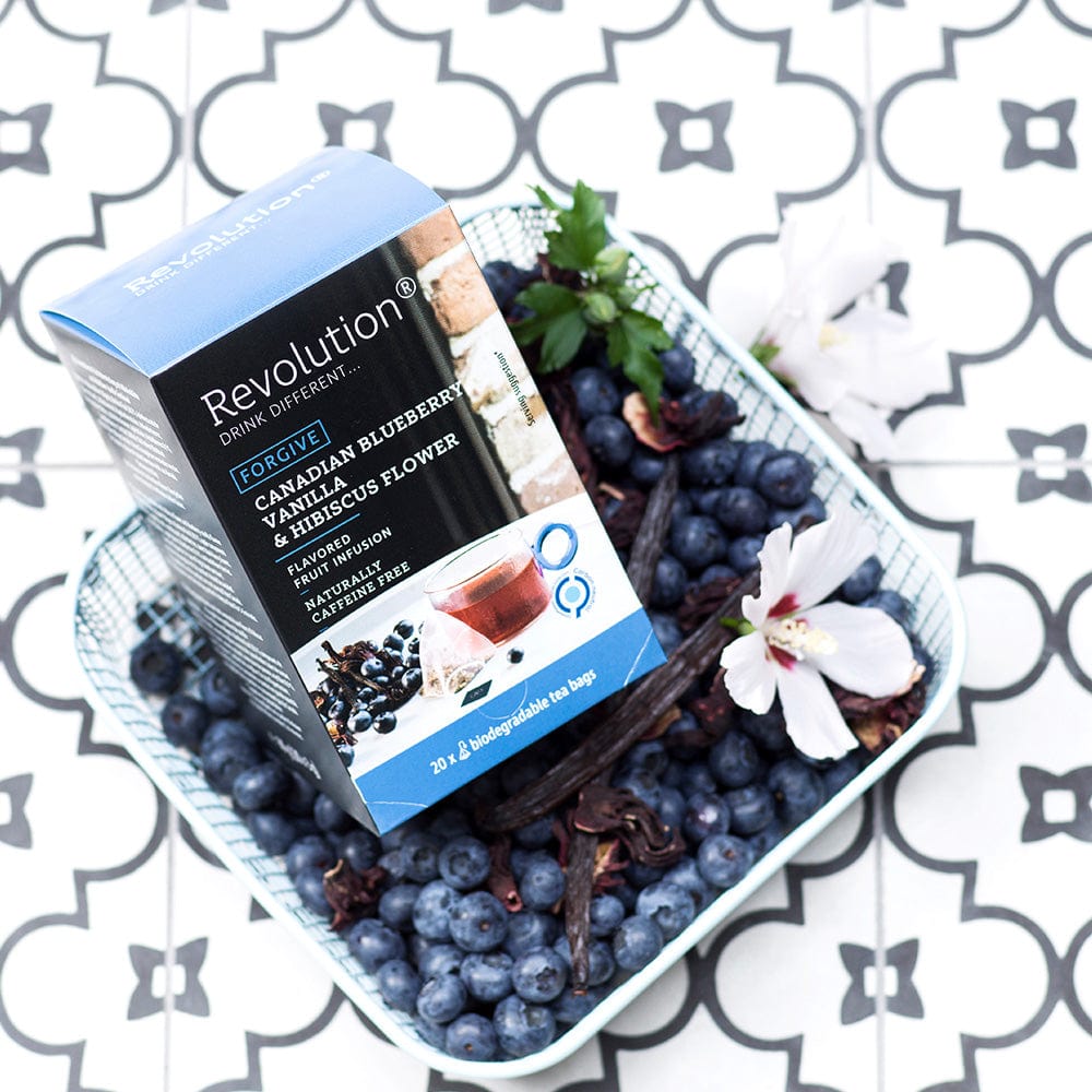 Box of Canadian Blueberry and Hibiscus tea surrounded by blueberries and white flowers.