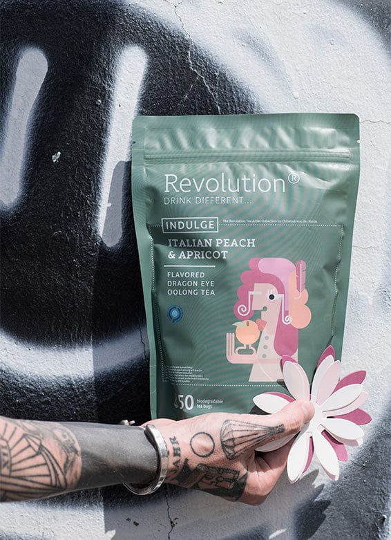 Tattooed hand holds Italian Peach & Apricot oolong tea pouch with a paper flower.