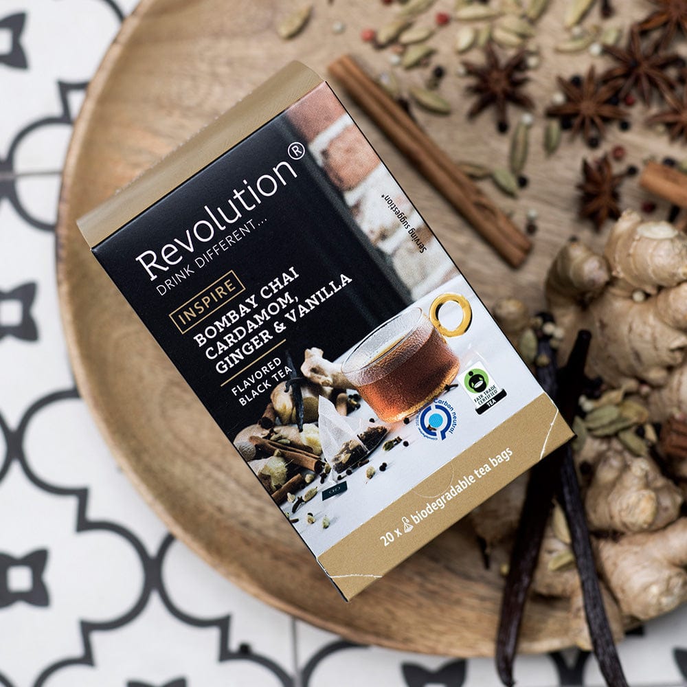 Bombay Chai tea box with ginger and vanilla, surrounded by spices on a wooden plate.