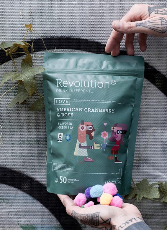Hands presenting American Cranberry & Rose flavored green tea, pom-poms in palm.