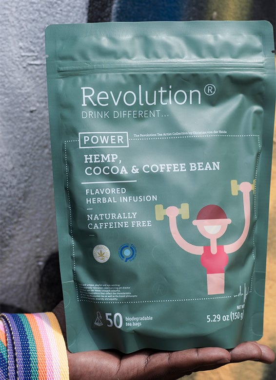 A hand holds a green tea pouch labeled 'Revolution' with hemp, cocoa, and coffee bean against graffiti.