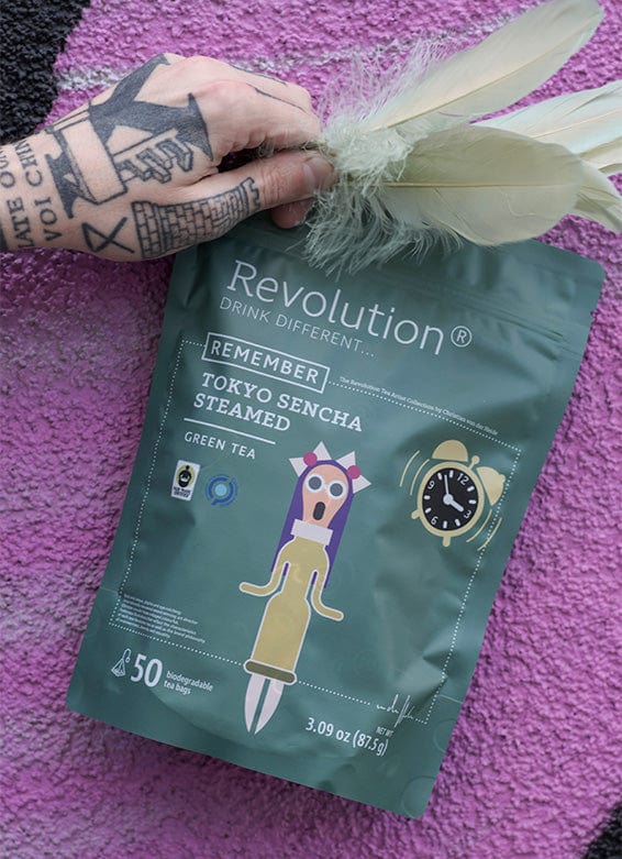 Hand with tattoos holds Tokyo Sencha Steamed green tea pouch against purple background.