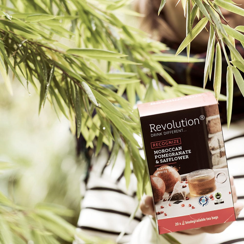 Box of Revolution Moroccan pomegranate and safflower tea held by hands, with foliage in foreground.