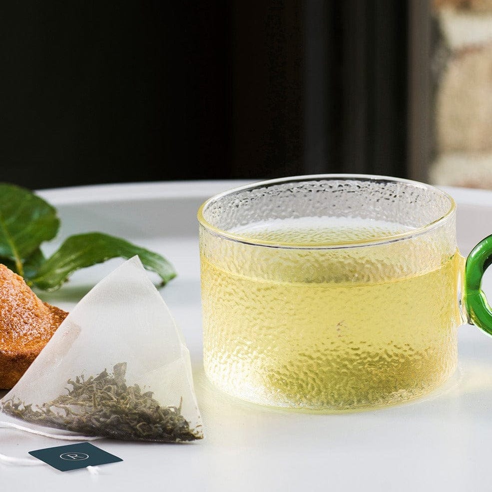 Glass of yellow tea and a tea bag on a white tray with blurred background.
