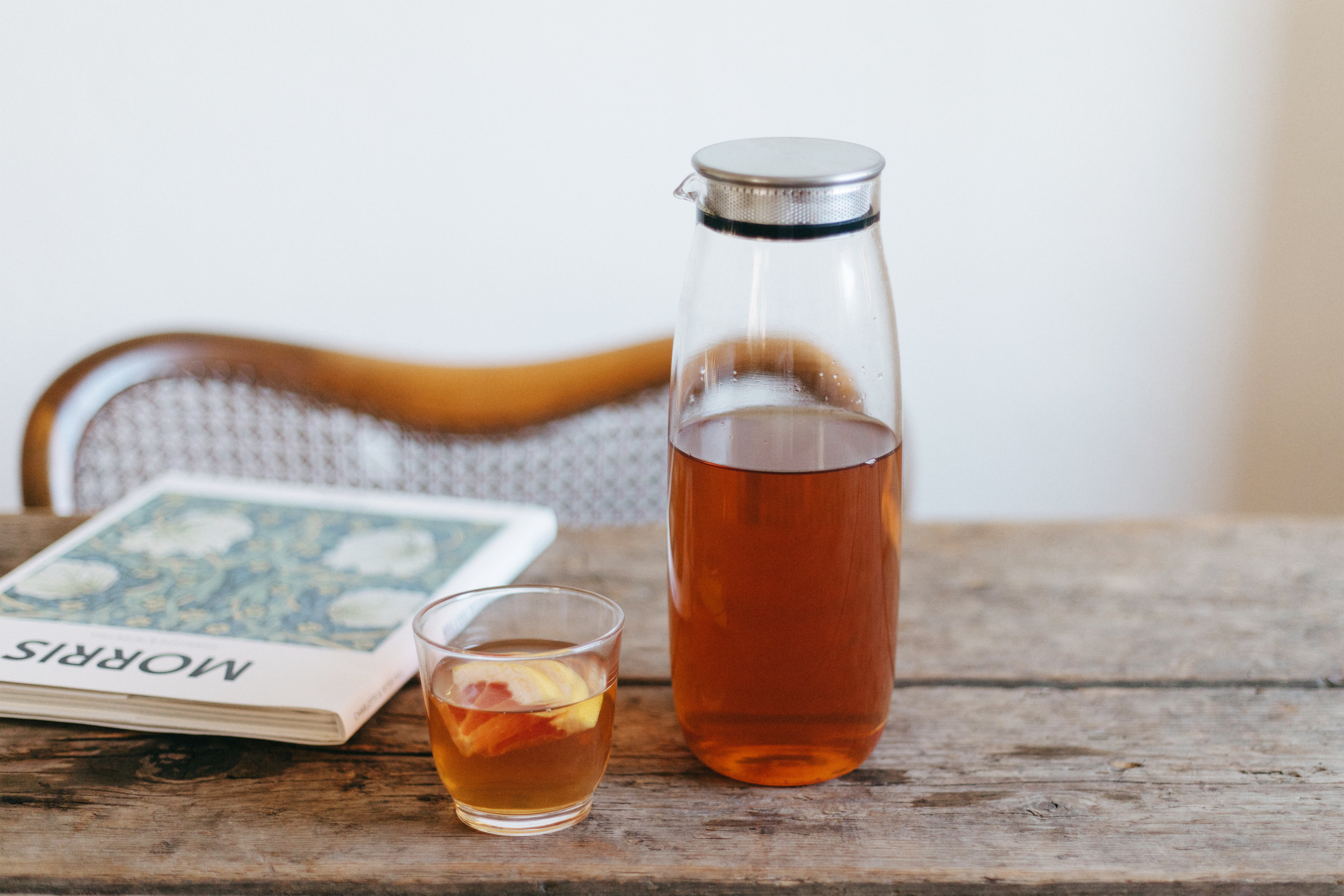 Wooden table holding a glass pitcher of iced tea and a cup, book to the side.