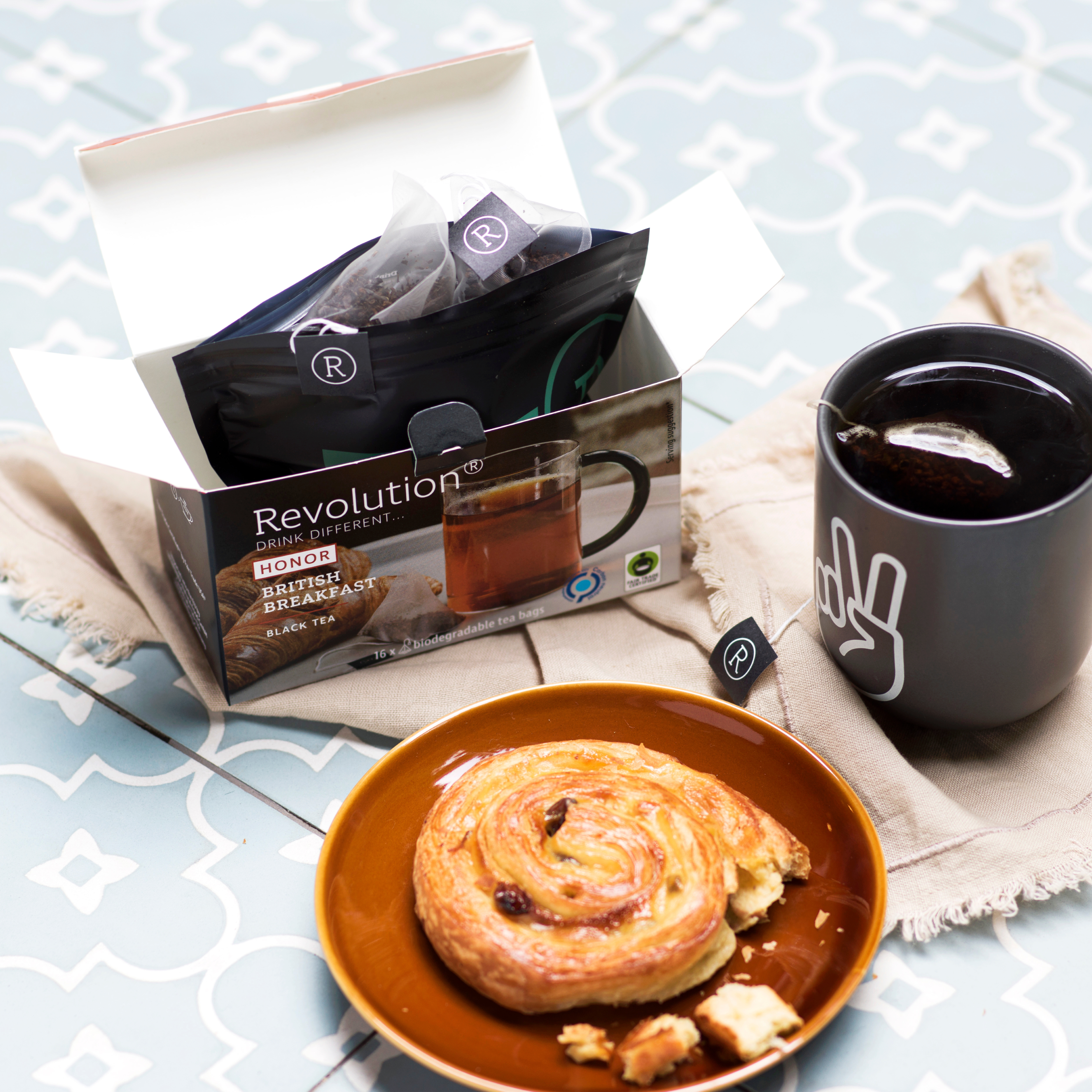 Tea box with a dark mug, pastry on plate, and cloth napkin.