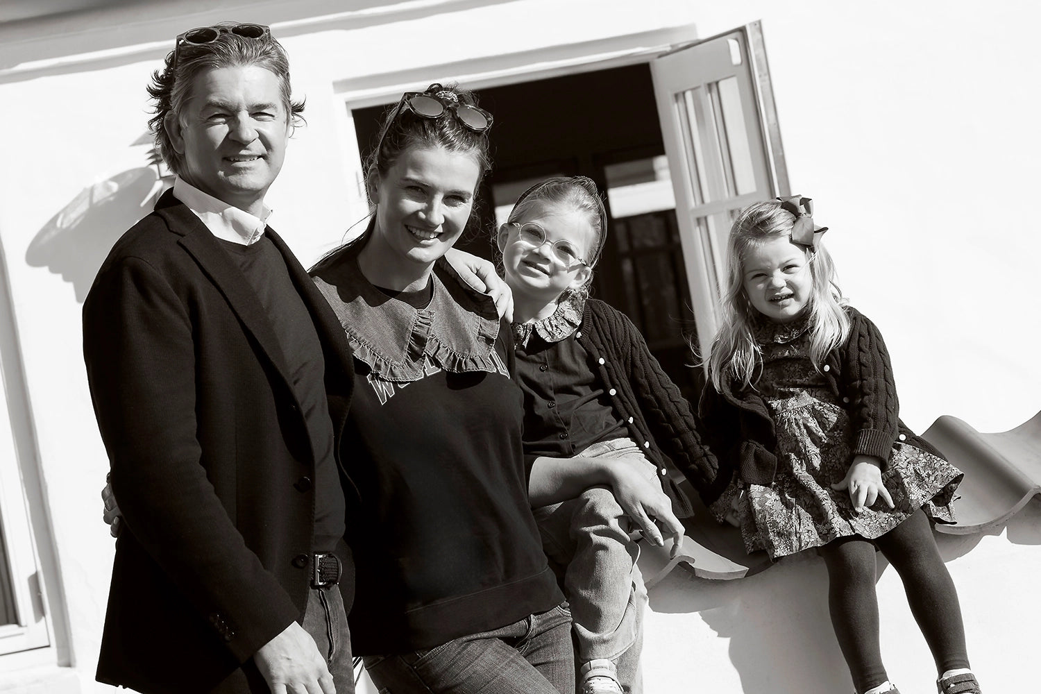 Black and white photo of a smiling family with two adults and two children outdoors.