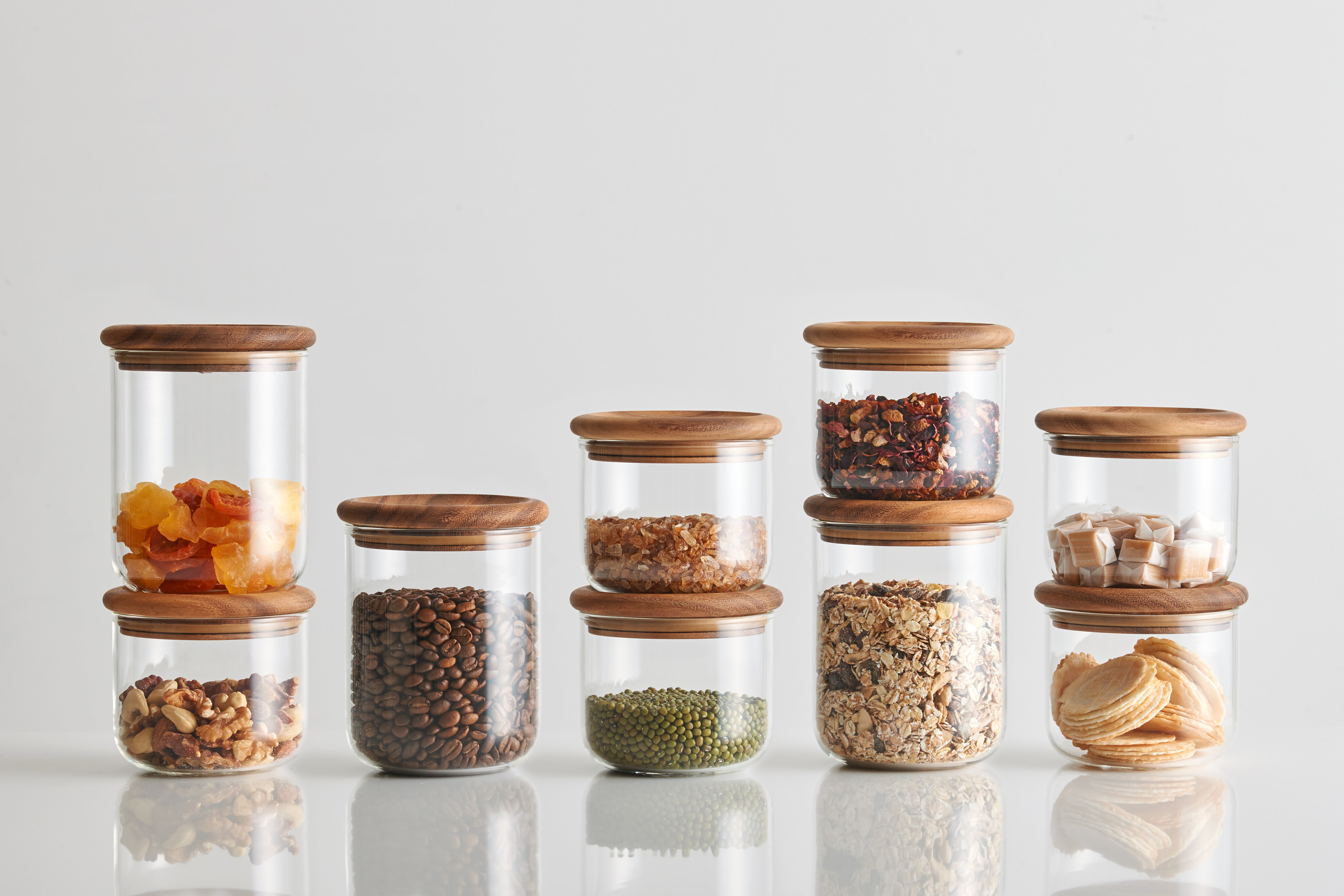 Nine clear jars with wooden lids filled with various dry goods.