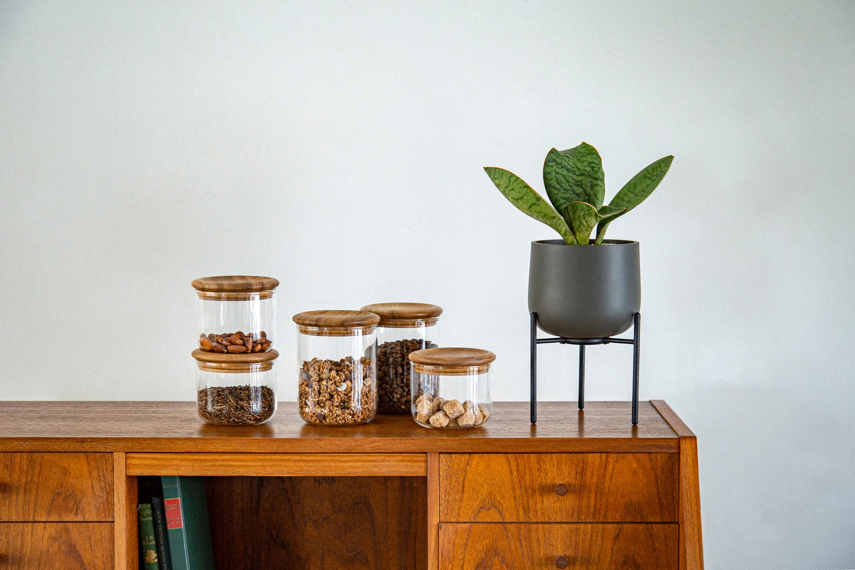 Wooden cabinet with glass jars of food and a potted plant on top.