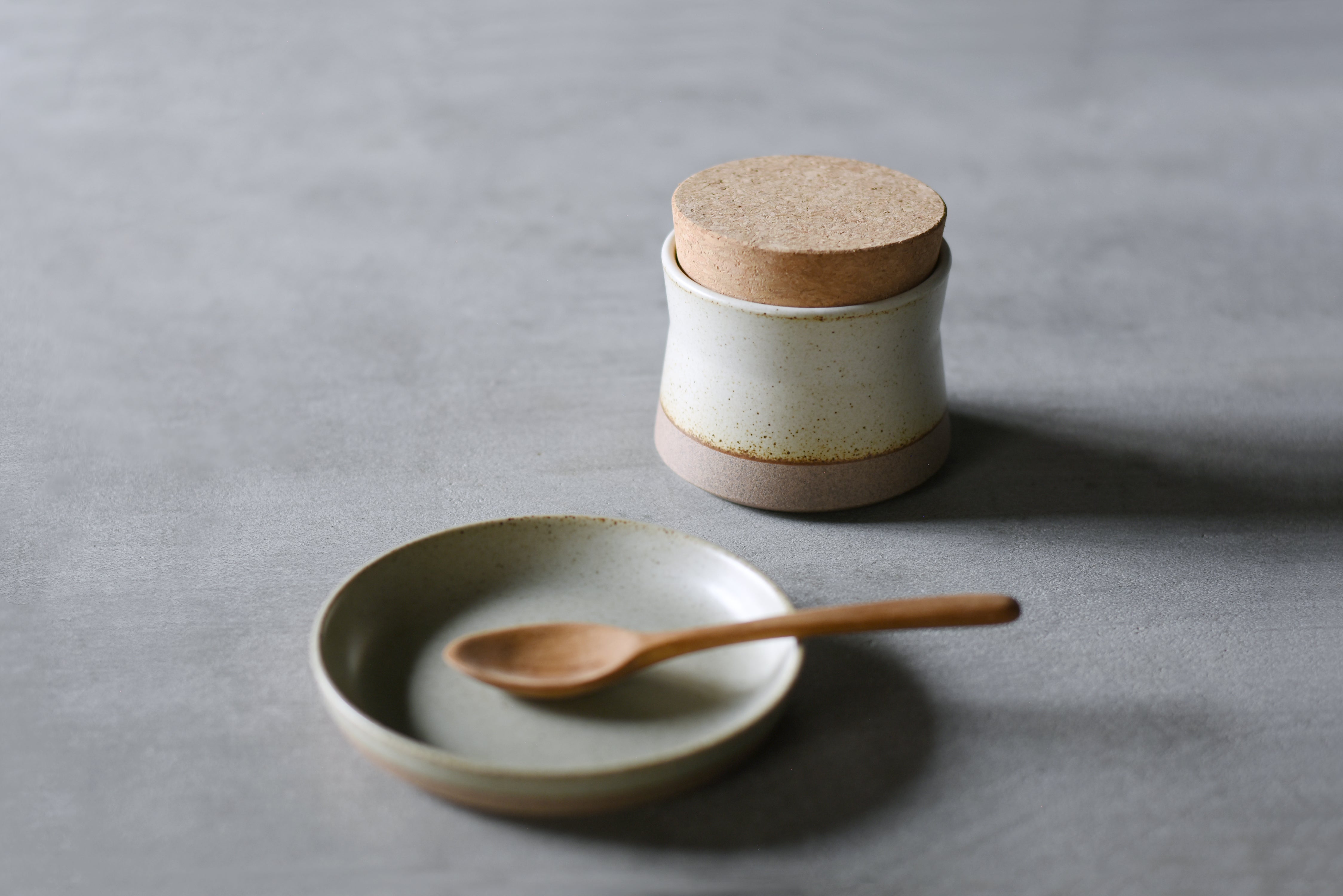 Ceramic jar with cork lid next to a plate and wooden spoon.