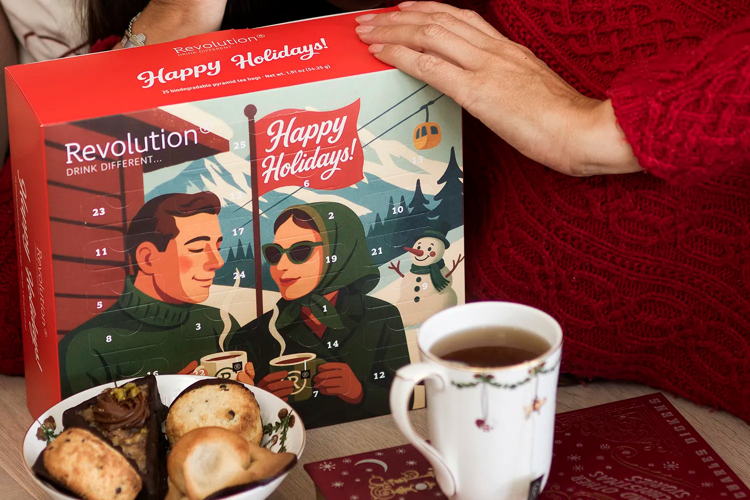 Zwei Personen genießen heiße Getränke. Auf dem Tisch ein Adventskalender, Gebäck und eine geschmückte Tasse.