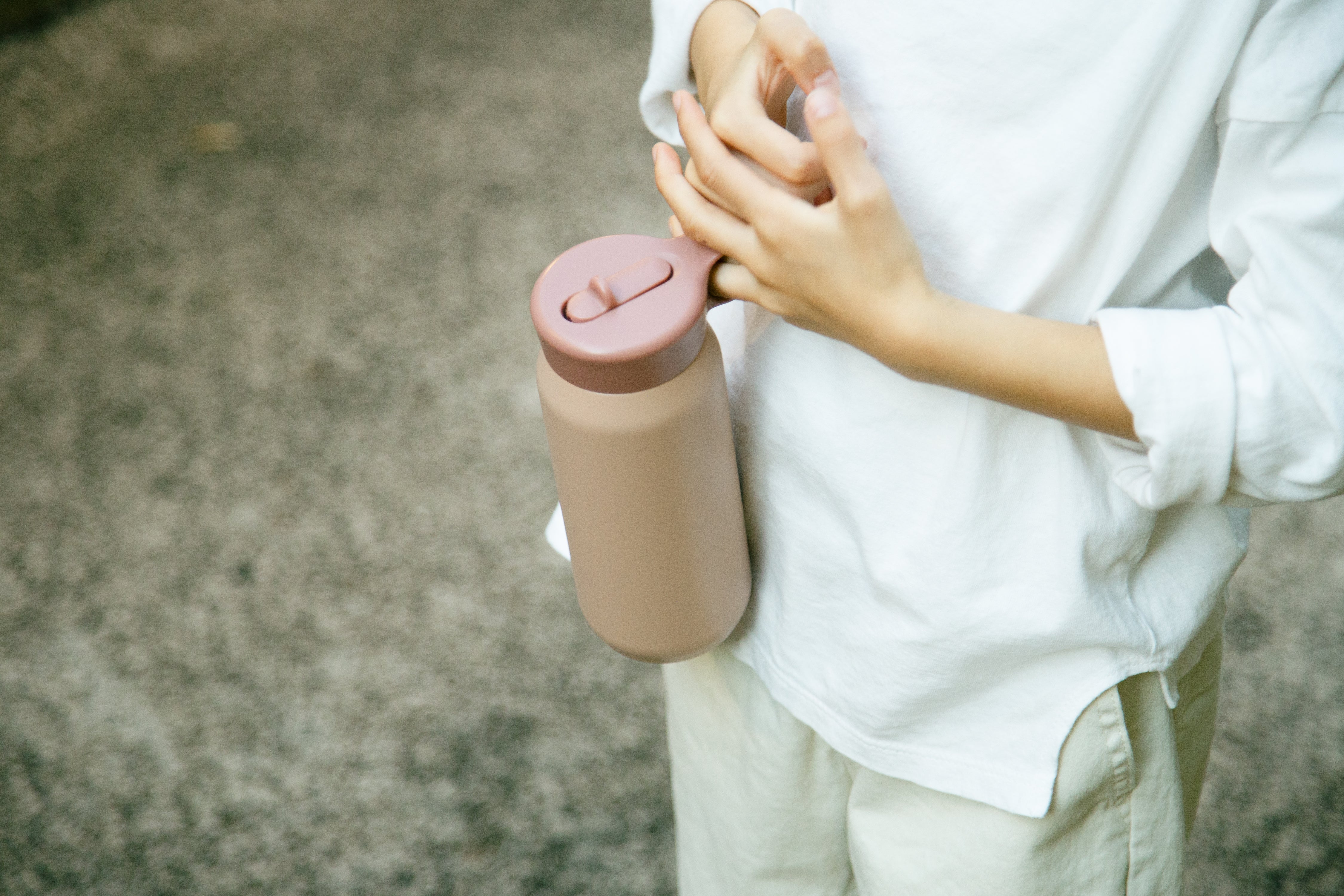 Person in white holding a pink bottle against their hip outdoors.