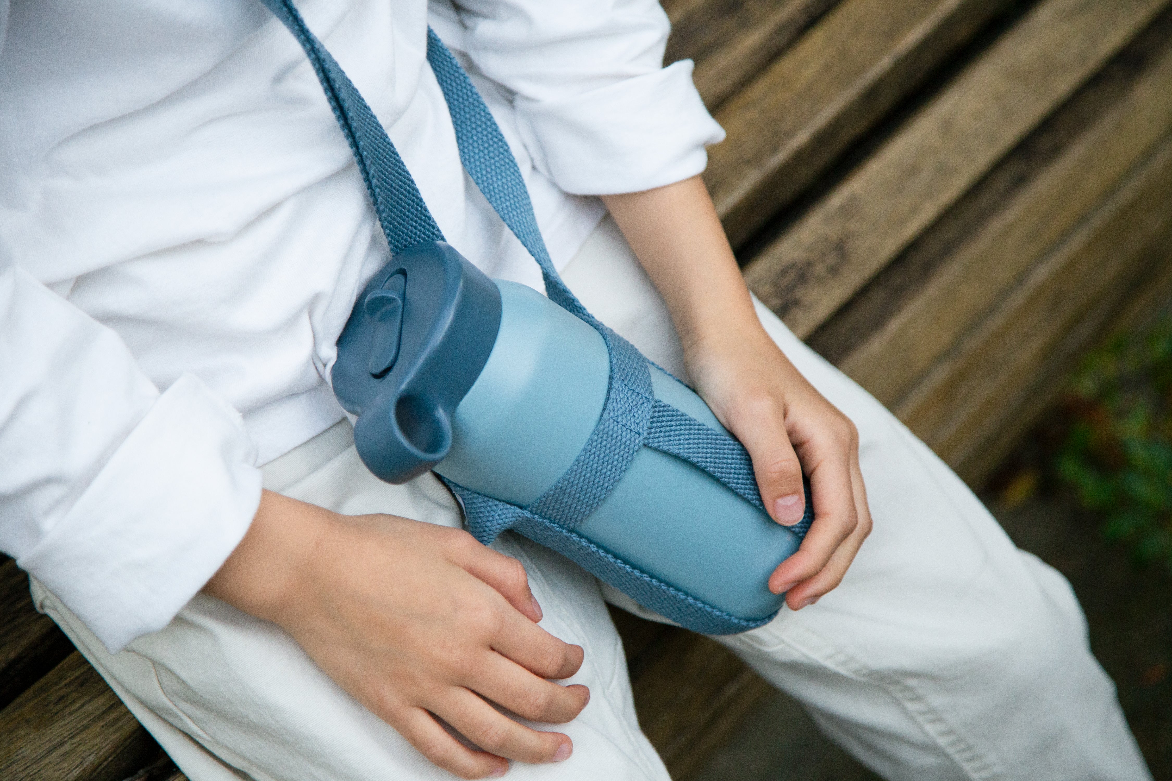 Person with white shirt sitting, holding a blue bottle with a strap.