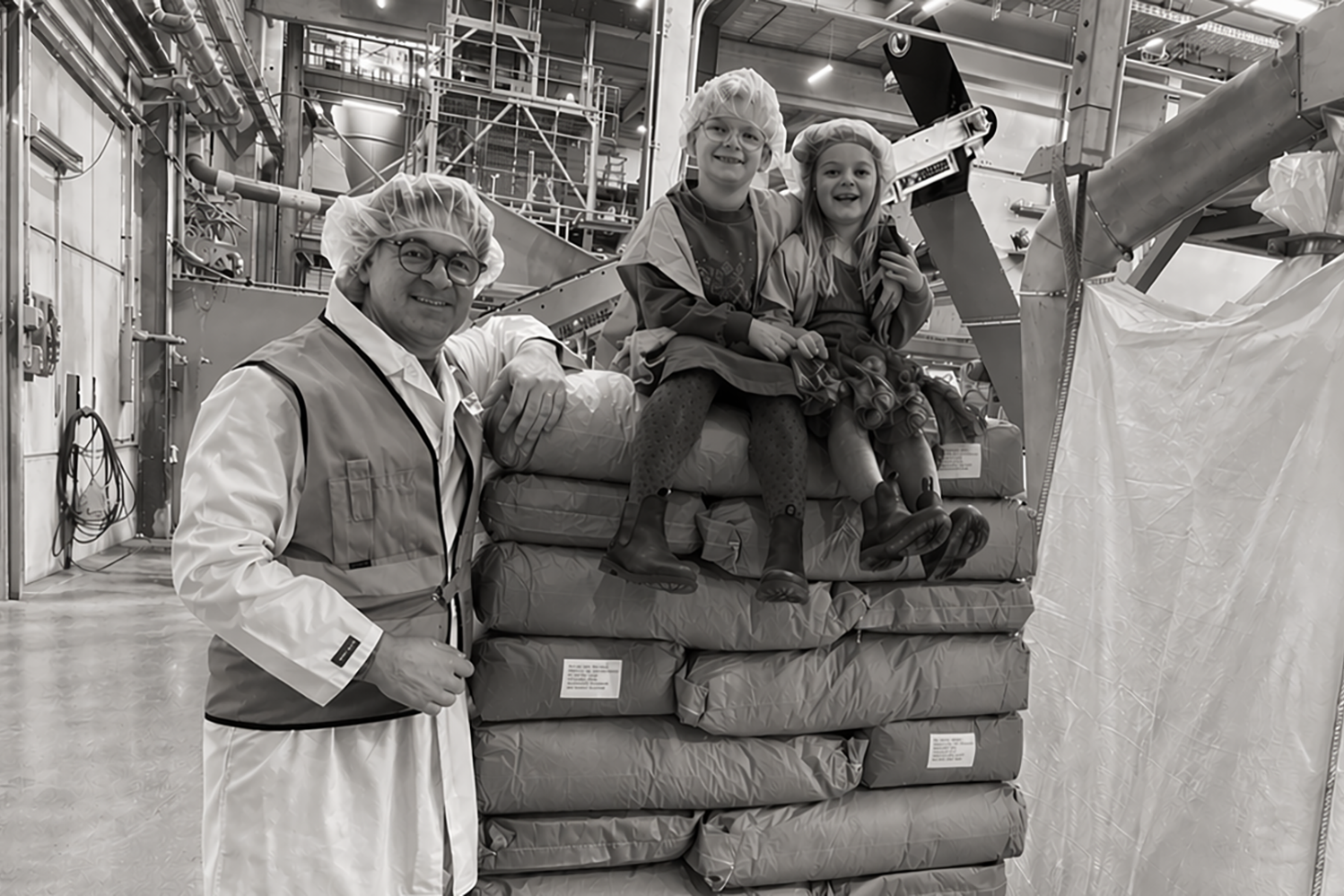 Person in uniform with two children sitting on stacked bags in an industrial setting.