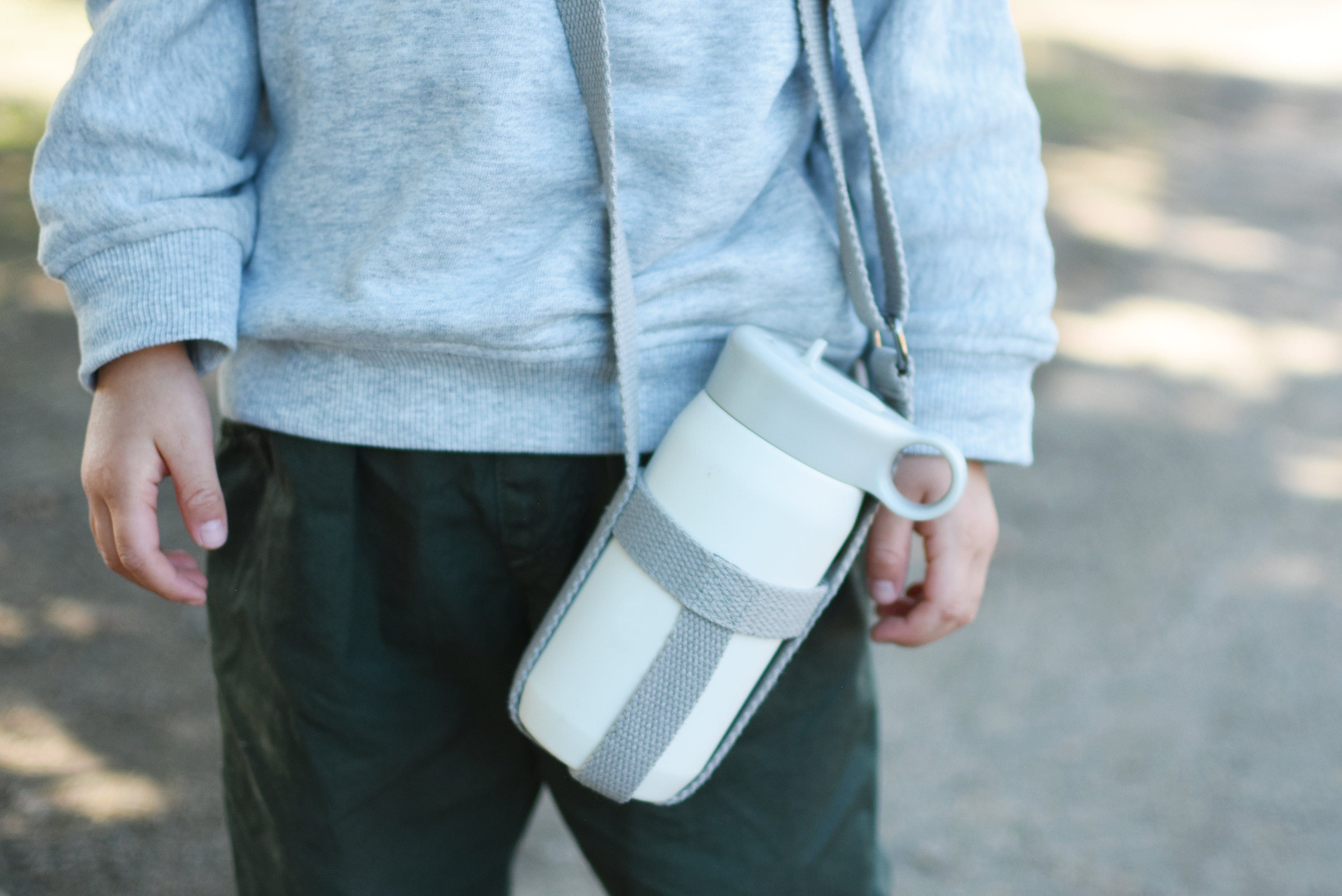 Child wearing a gray top and holding a white bottle in a gray sling.