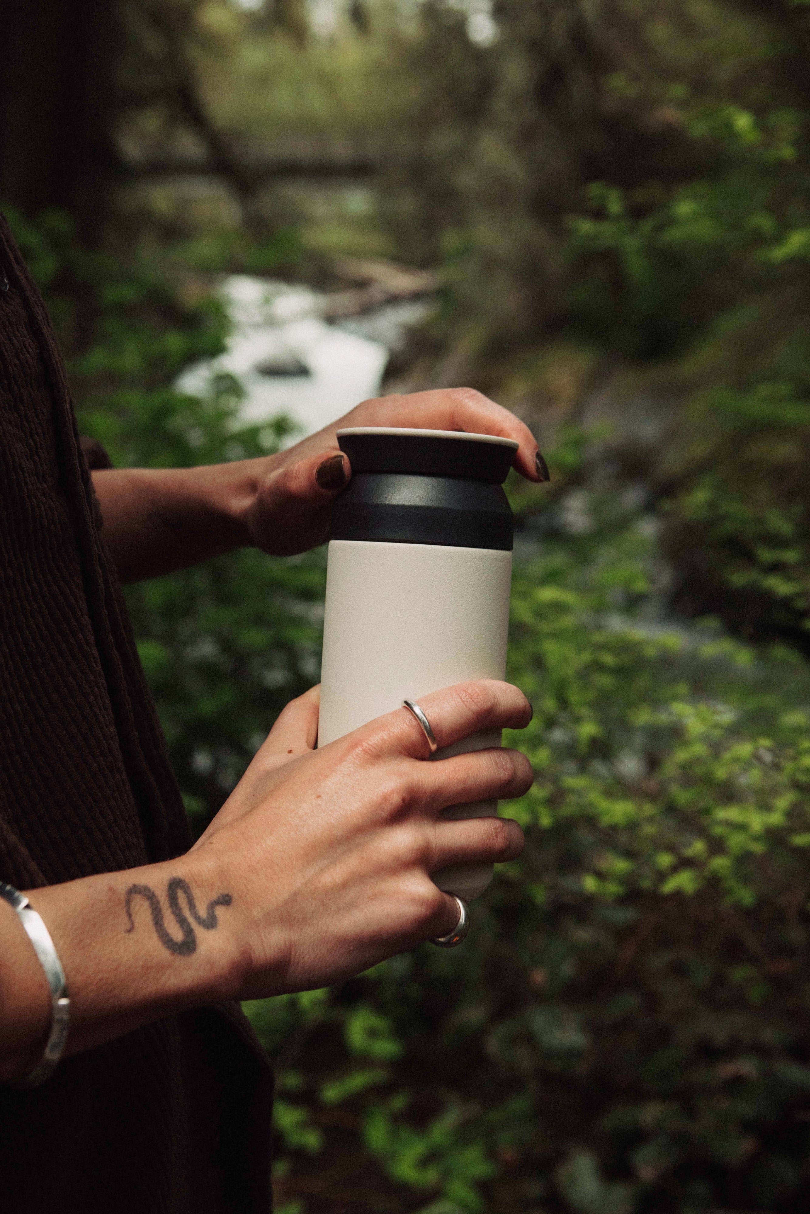 Person holding a travel mug with both hands in a natural outdoor setting.