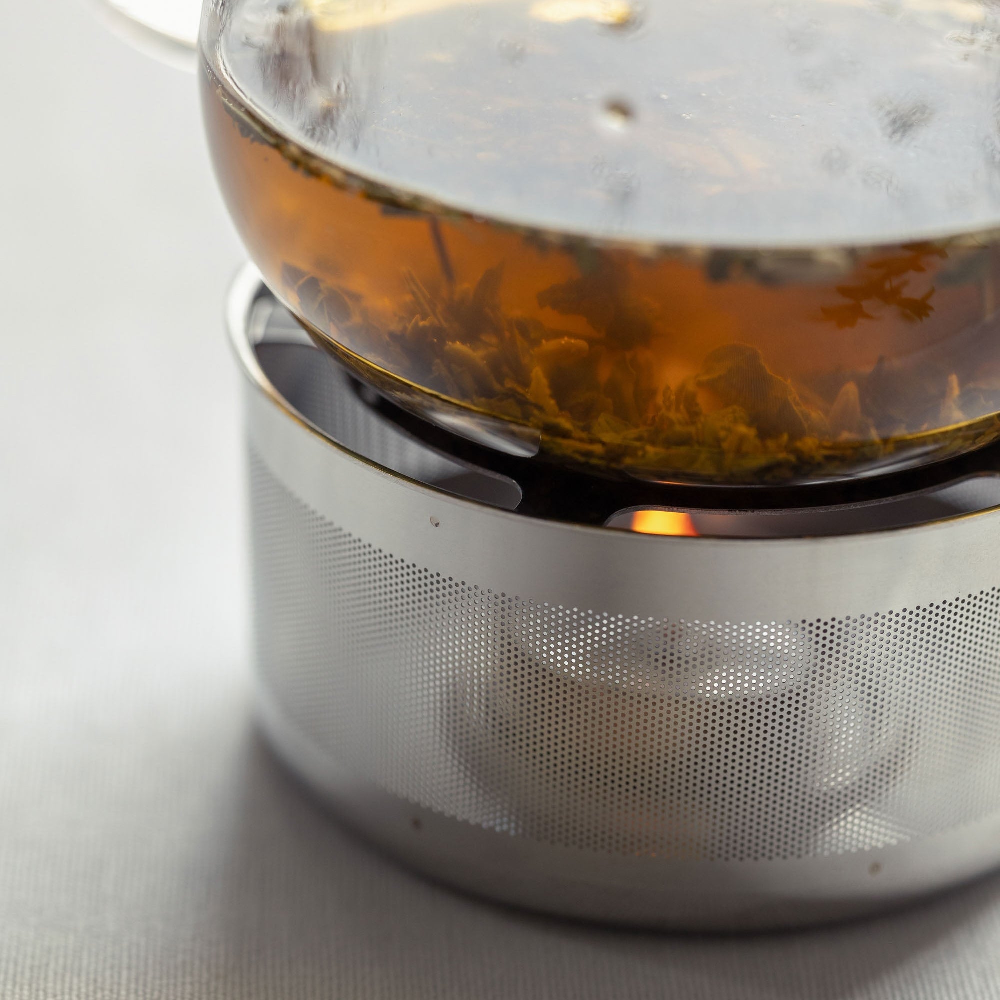 Close-up of glass teapot on metal warmer with lit candle inside.