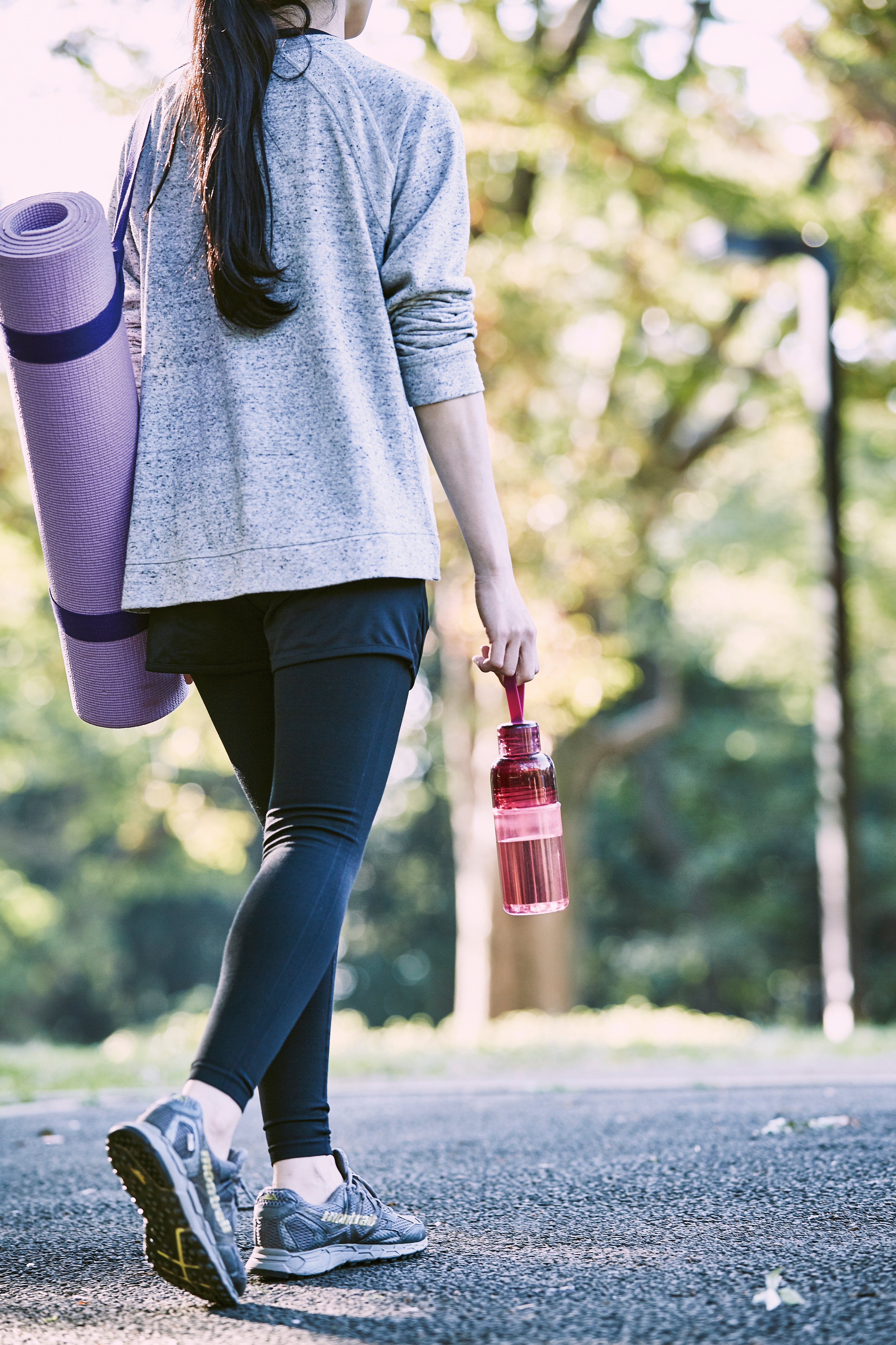 Person in sportswear holding a pink water bottle on a leafy path.