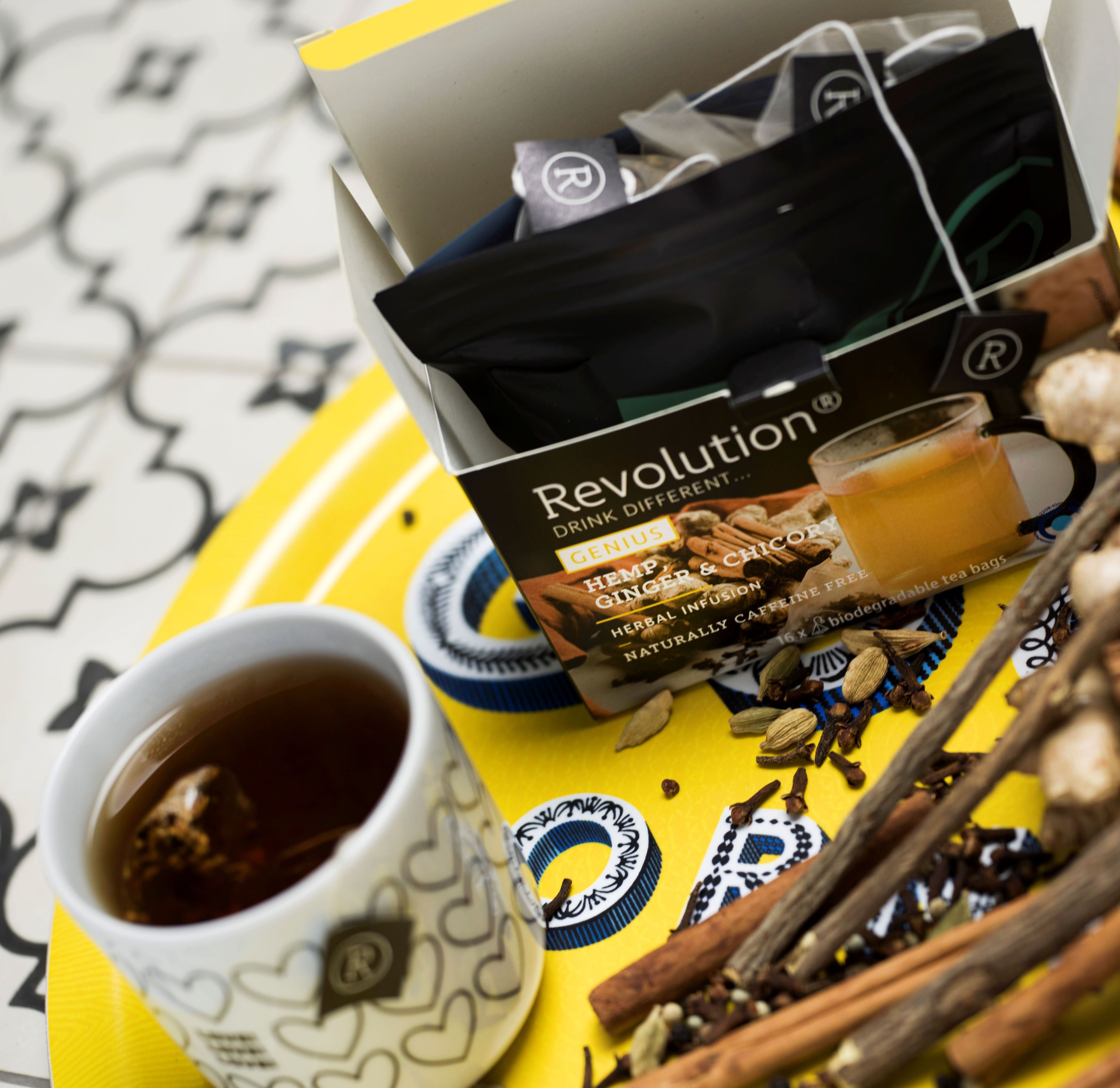 Open tea box and mug on a yellow tray with spices and tea leaves.