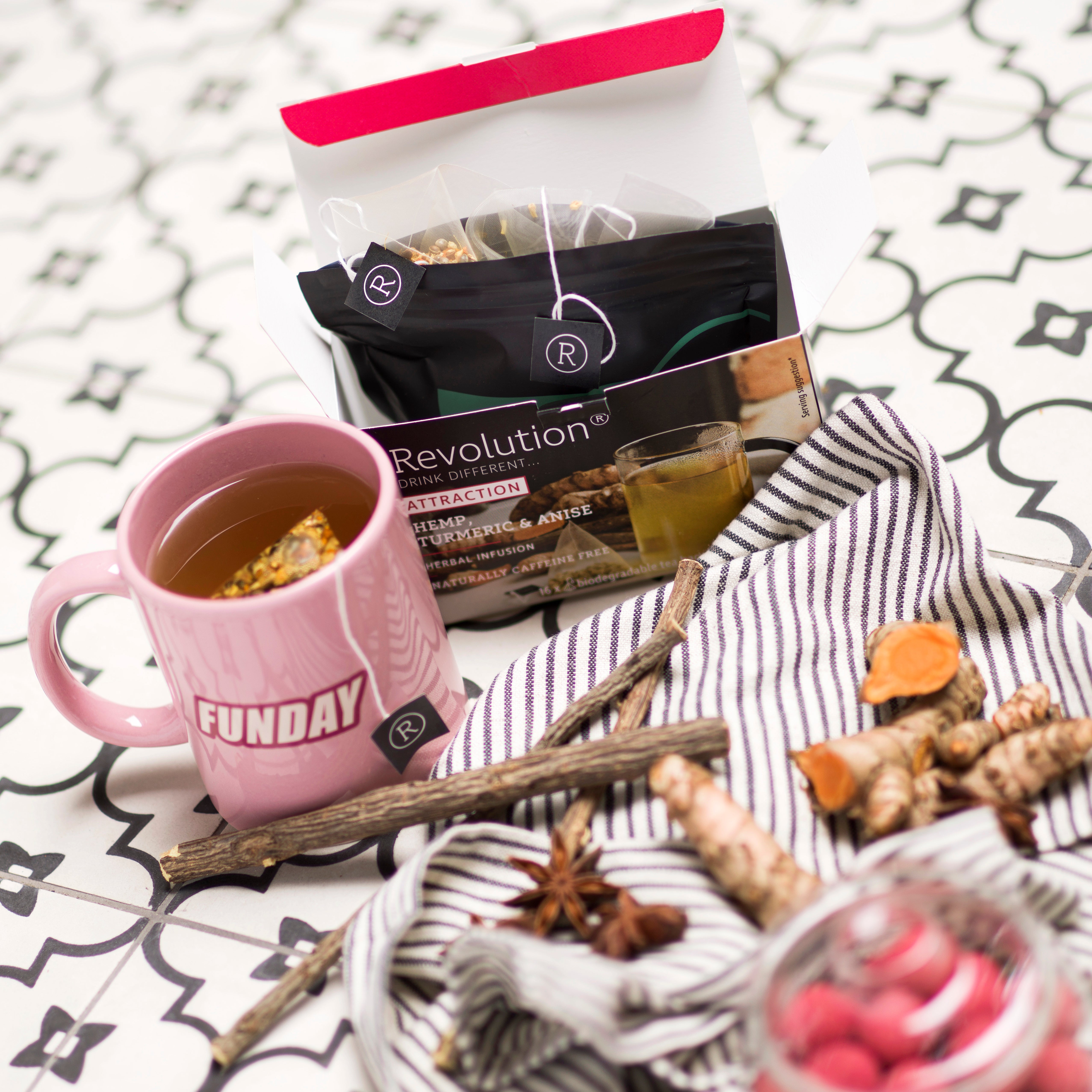 Tea box, pink mug, spices, and cloth on patterned tile.