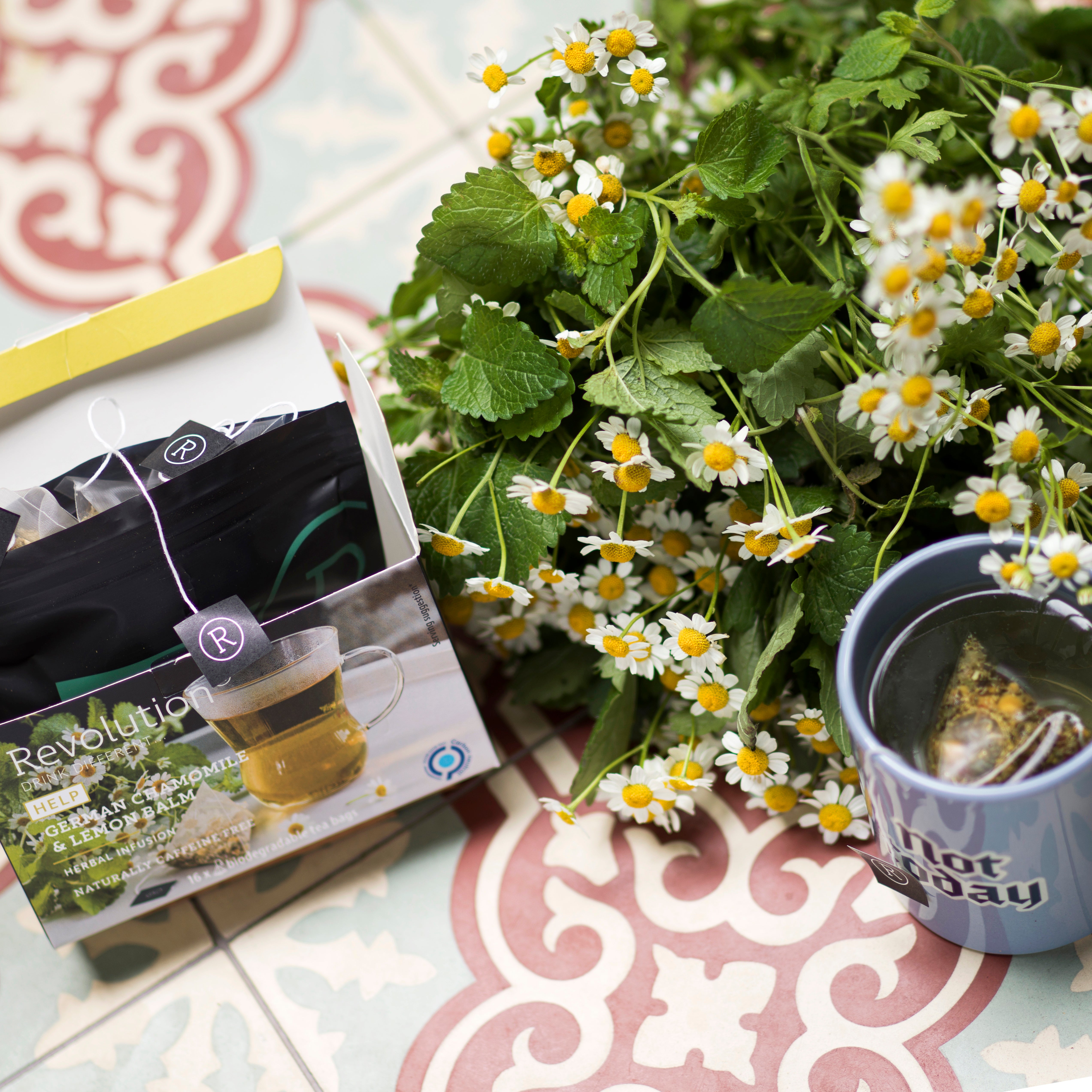 Tea box, flowers, and blue mug on red patterned tile.