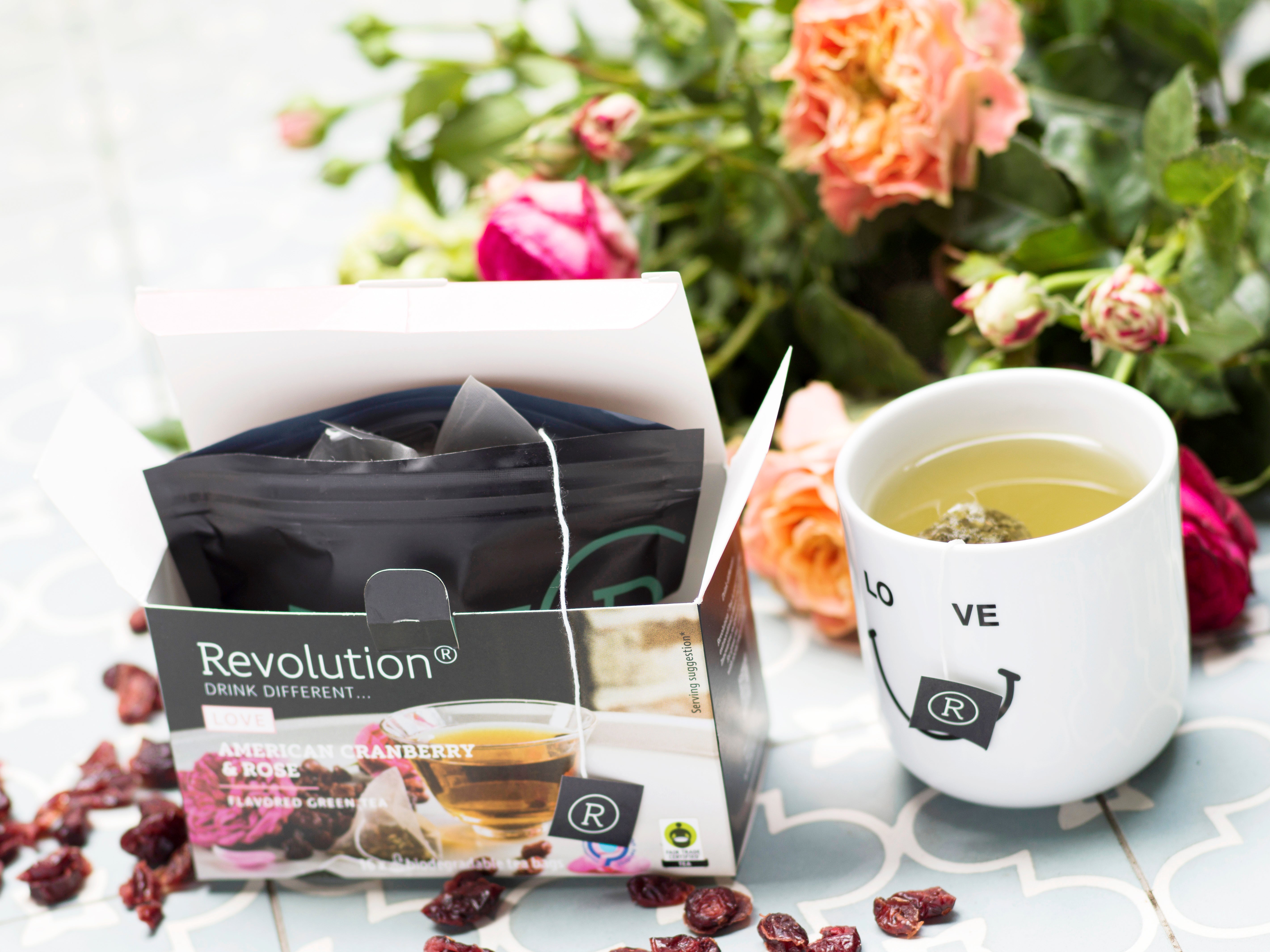 Open tea box, flowers, and mug with tea on a tiled surface.