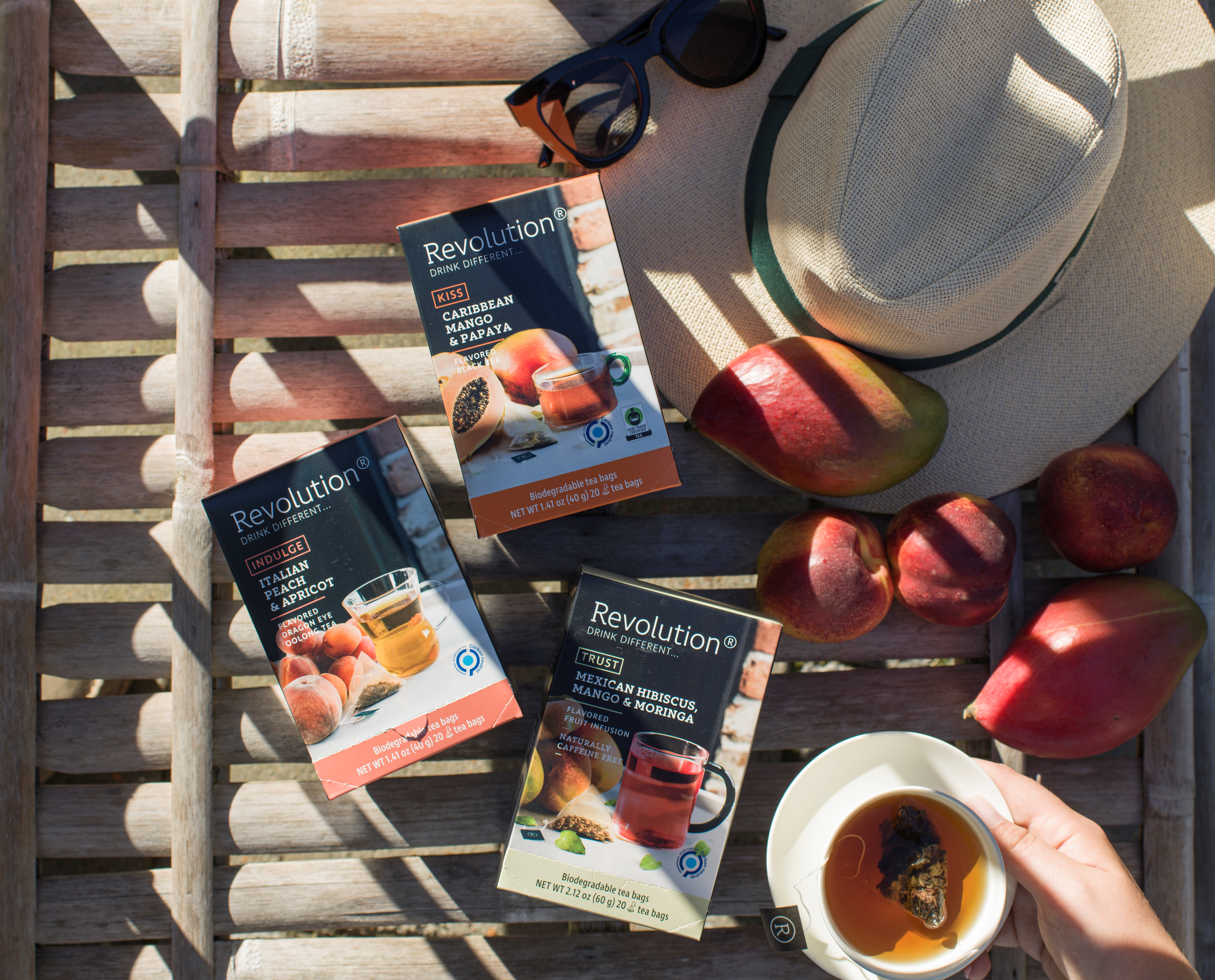 Three boxes of tea on a wooden bench with peaches and sunglasses nearby.