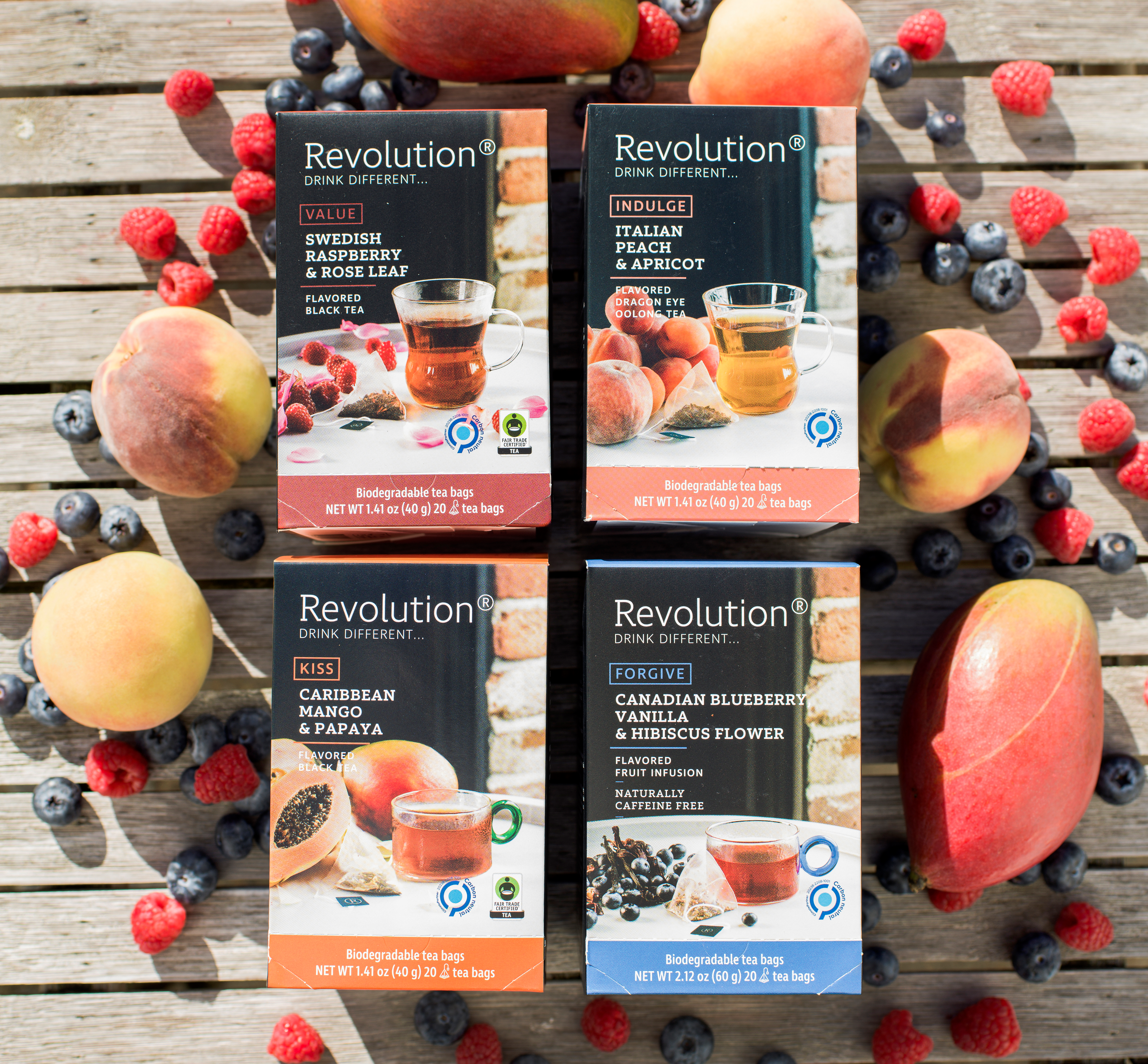 Four boxes of tea on a wooden surface surrounded by berries and peaches.