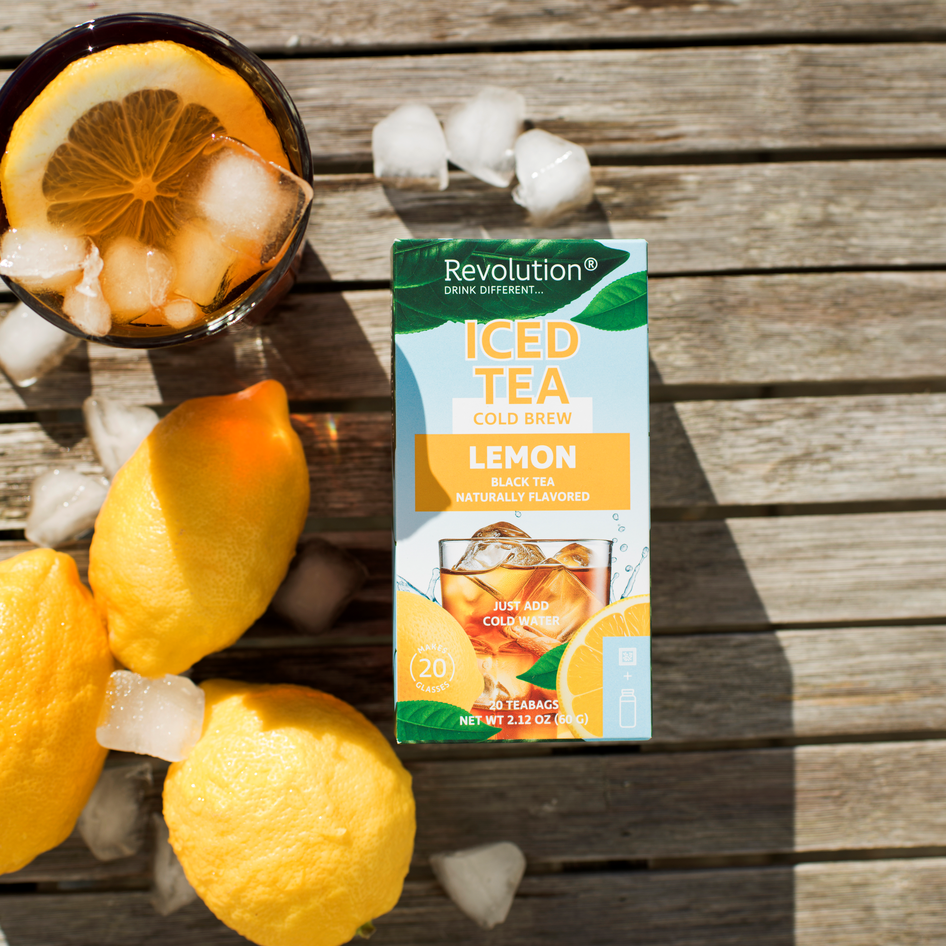 Iced tea with lemon slices; tea box and whole lemons on a wooden surface with ice cubes.