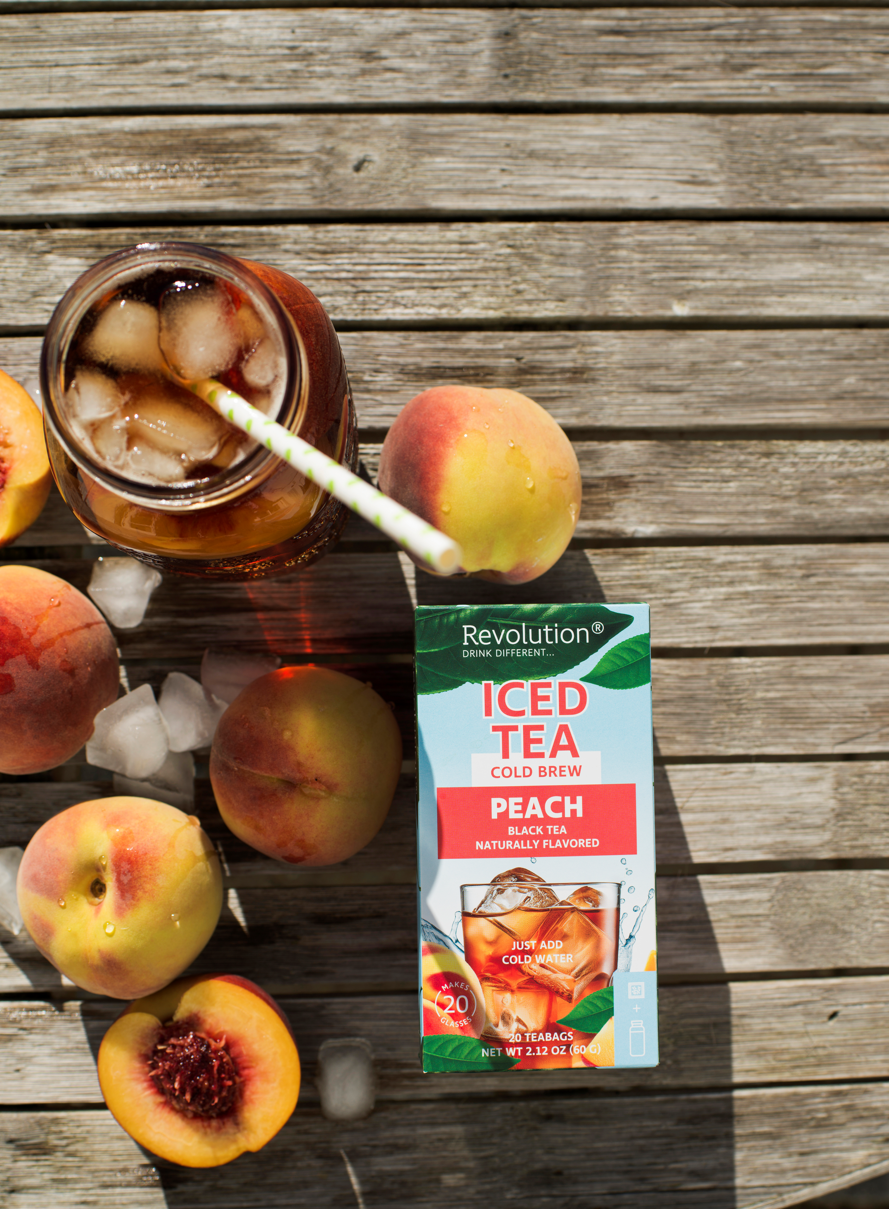 Iced tea with a straw; peach iced tea box and whole peaches on a wooden surface with ice cubes.