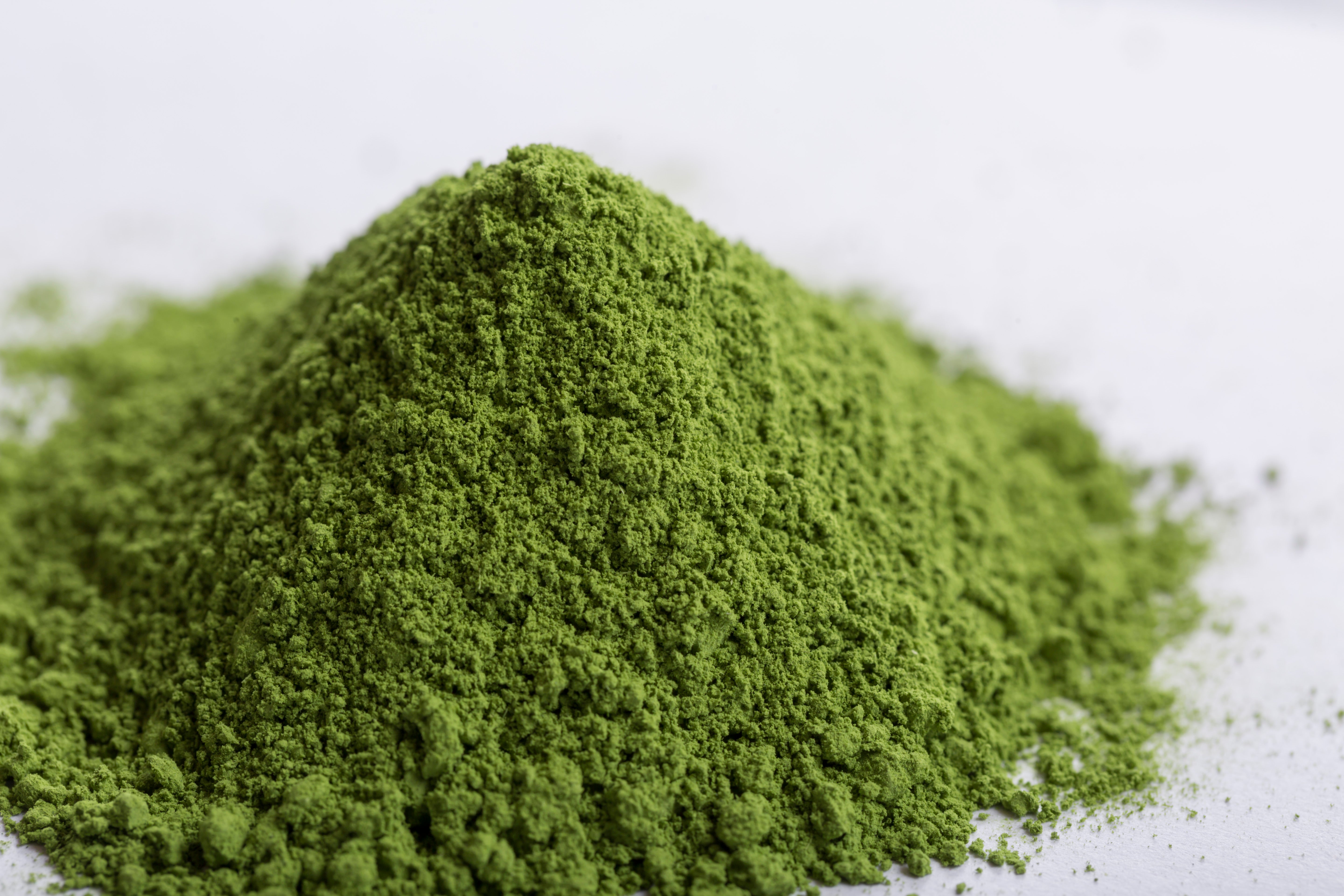 Heaped green matcha powder on a white surface, showing smooth texture.