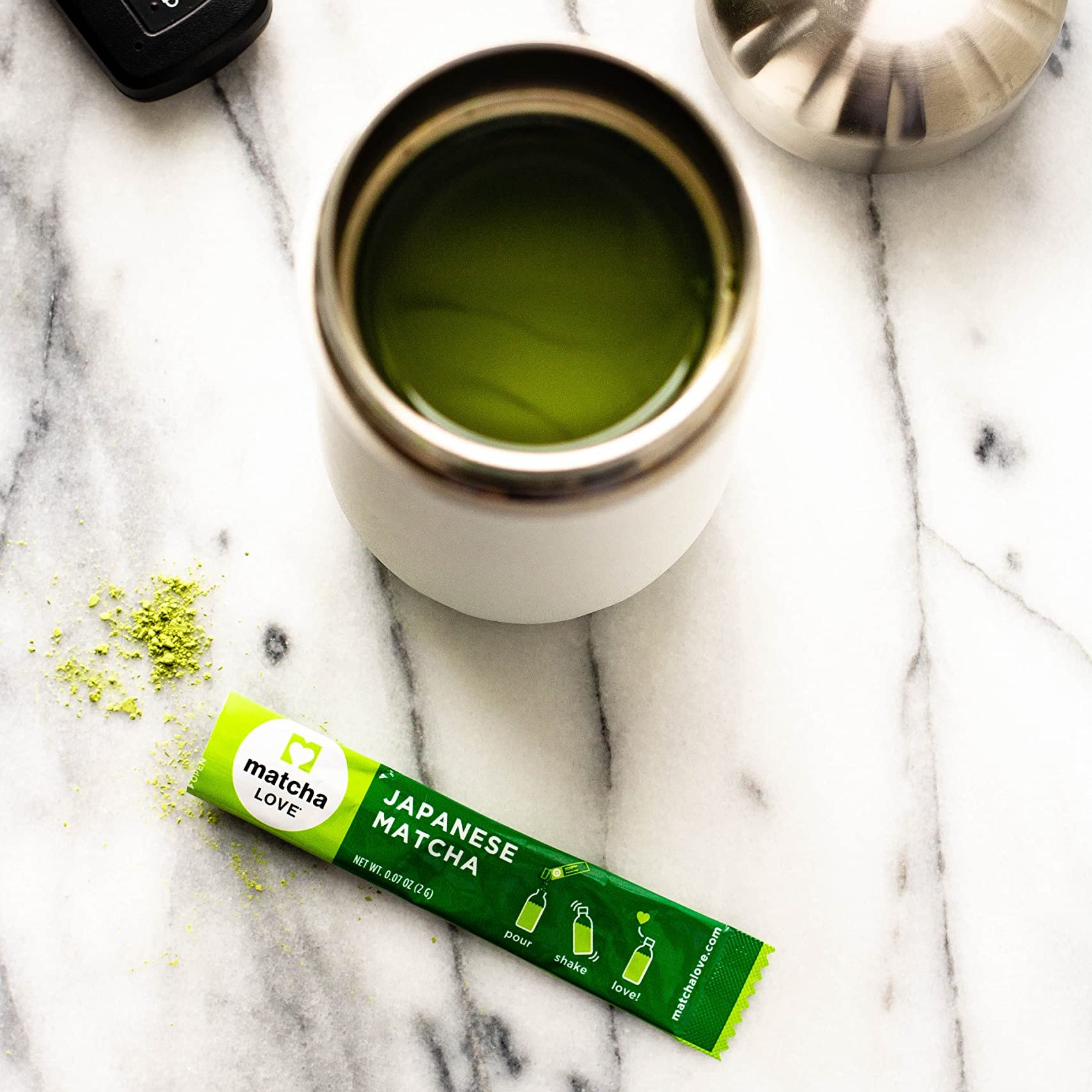 Green matcha stick next to a thermos on marble with car keys and lid nearby.