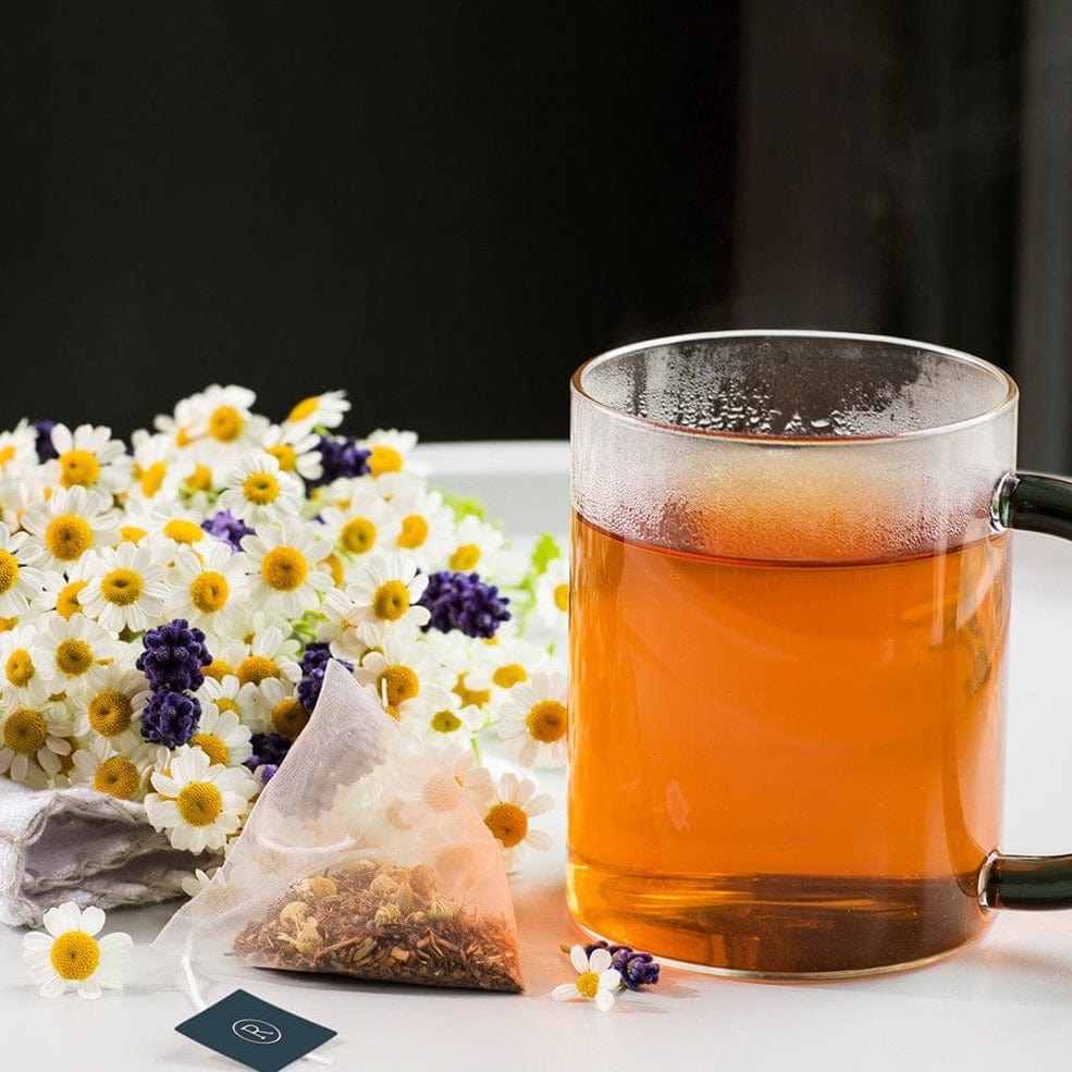 Glass mug with chamomile flowers and tea bag.