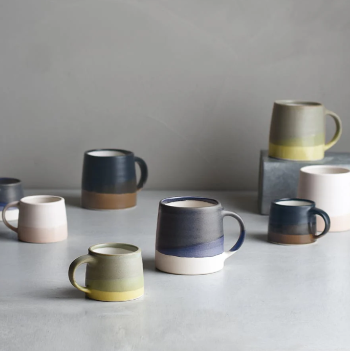 Ceramic mugs in various colors and sizes arranged on a gray surface.