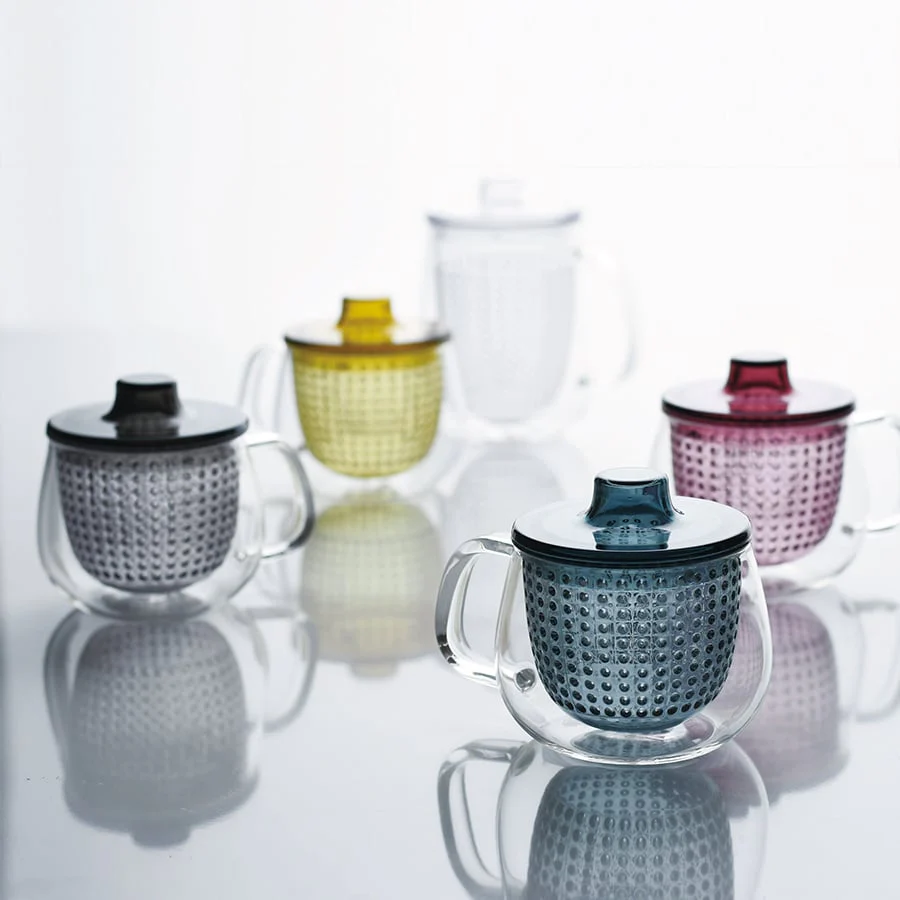 Five glass mugs with colorful lids and infusers on a reflective surface.