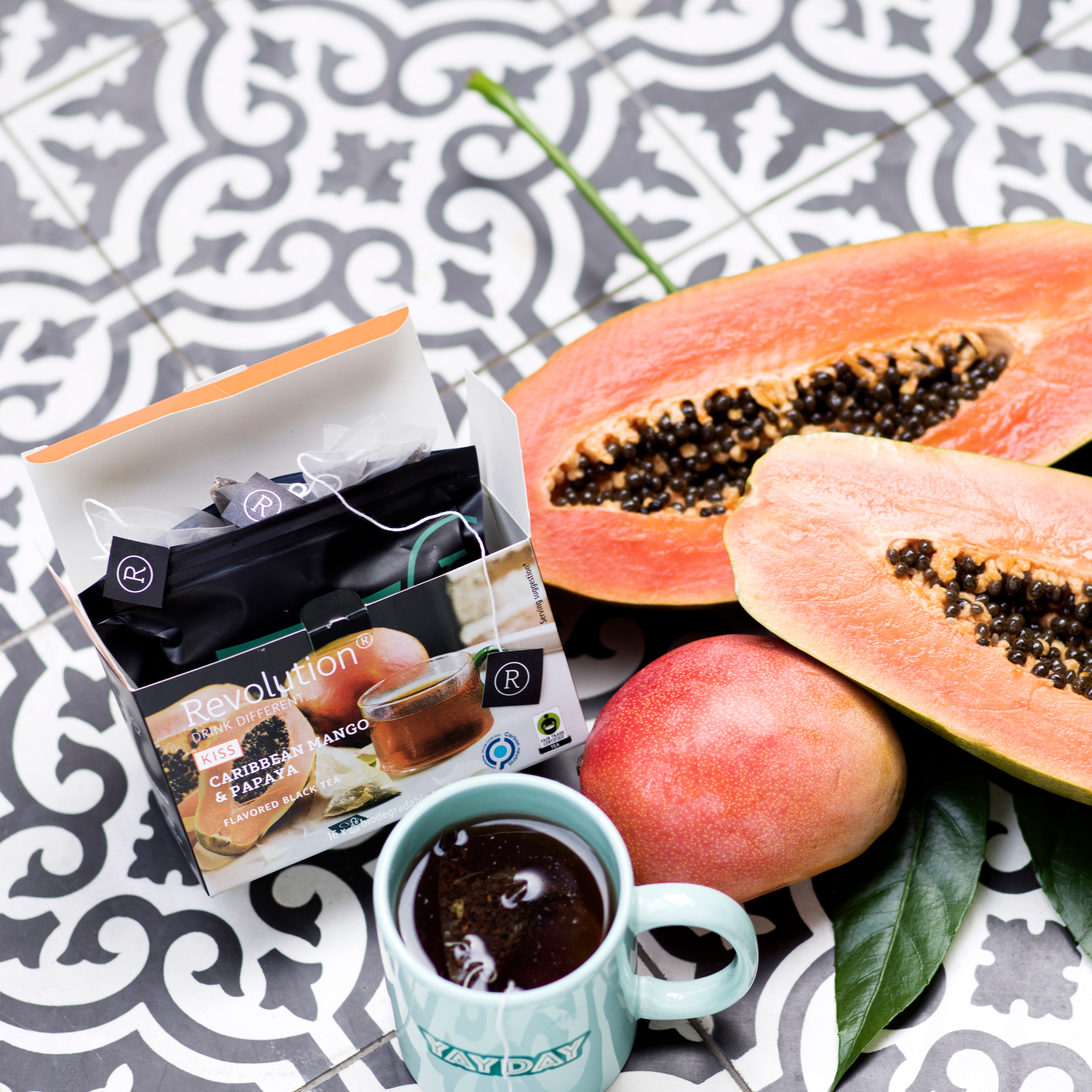 Tea box with a halved papaya, a mango, and a cup on patterned tiles.