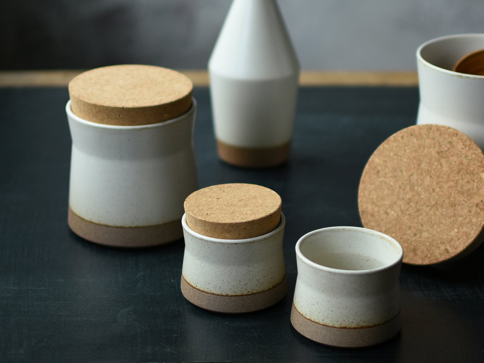 Set of ceramic containers with cork lids on a dark surface.