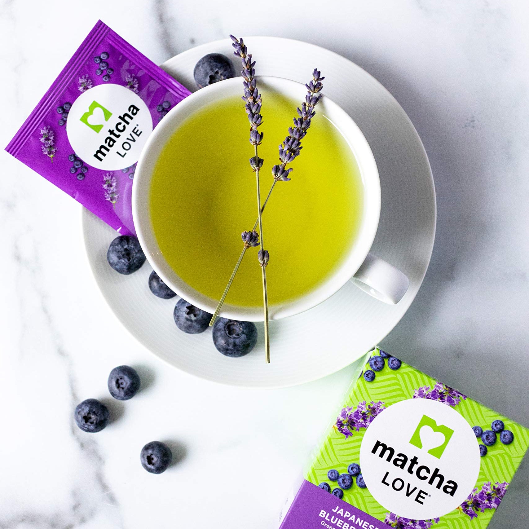 Cup of green tea with lavender garnish, blueberries, and tea packets.