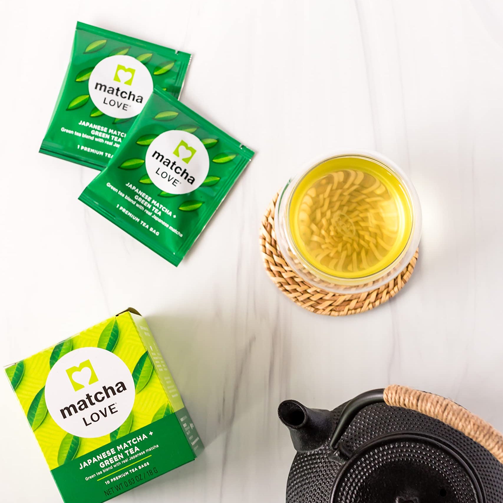 Wooden surface with kettle, tea packets, box, and cup of green tea.