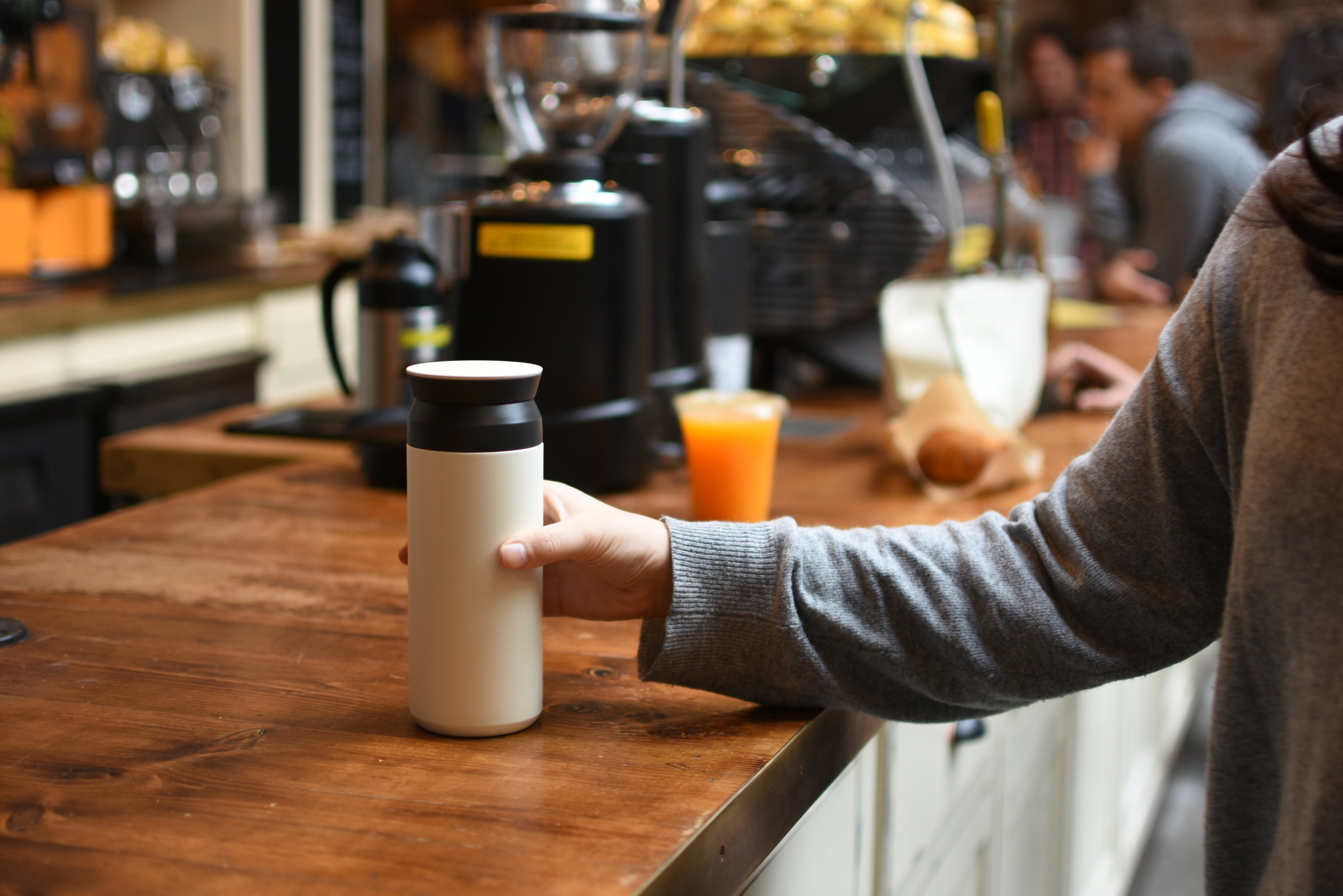 Person holding a travel mug at a wooden countertop in a café setting.