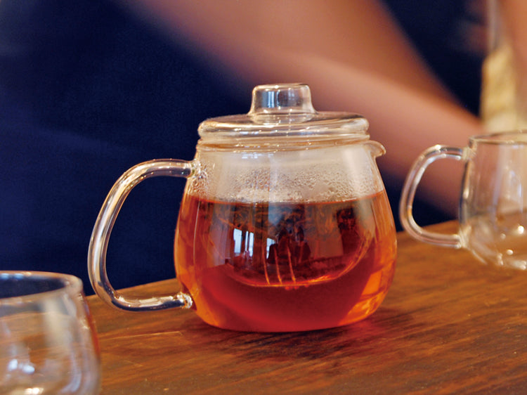 Glass teapot with amber tea inside on wooden table.