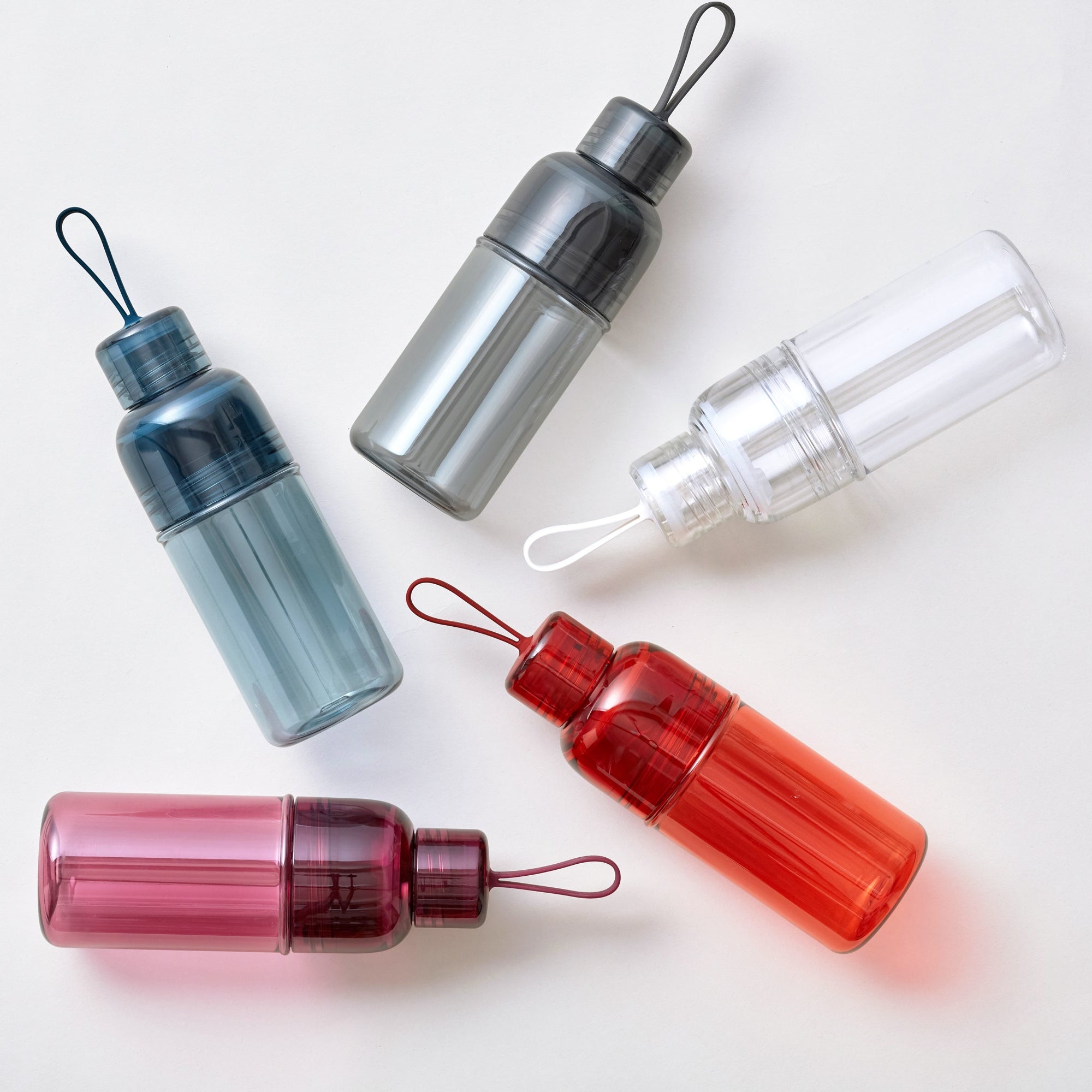 Five colorful water bottles with loop handles on a light surface.